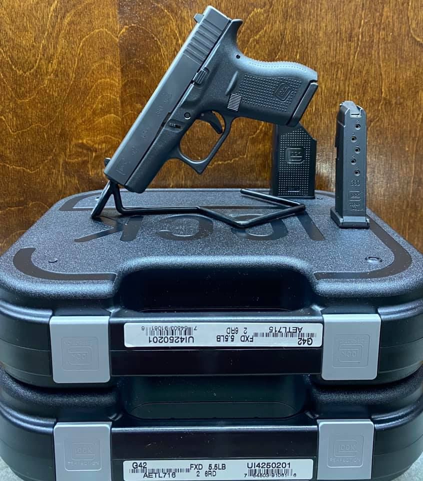 Black handgun displayed atop stacked black cases with a magazine beside it on a wooden surface