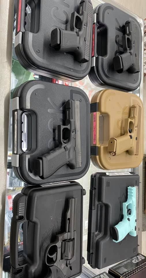 Stacked hard cases with handguns displayed inside, including black, tan, and mint-green firearms.