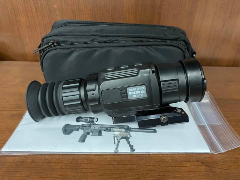 Black handheld thermal scope on a table with a black pouch and small parts beneath it