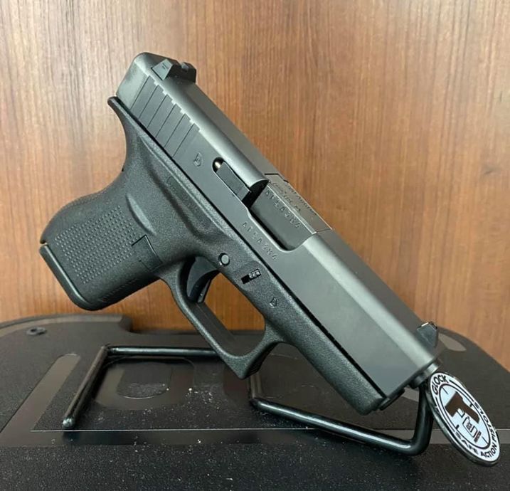 Black semi-automatic handgun displayed on a stand against a wooden background.