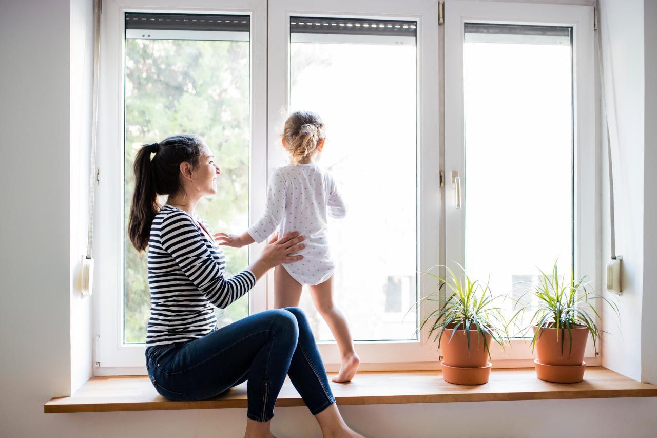 A woman and a child are sitting on a window sill looking out the window.