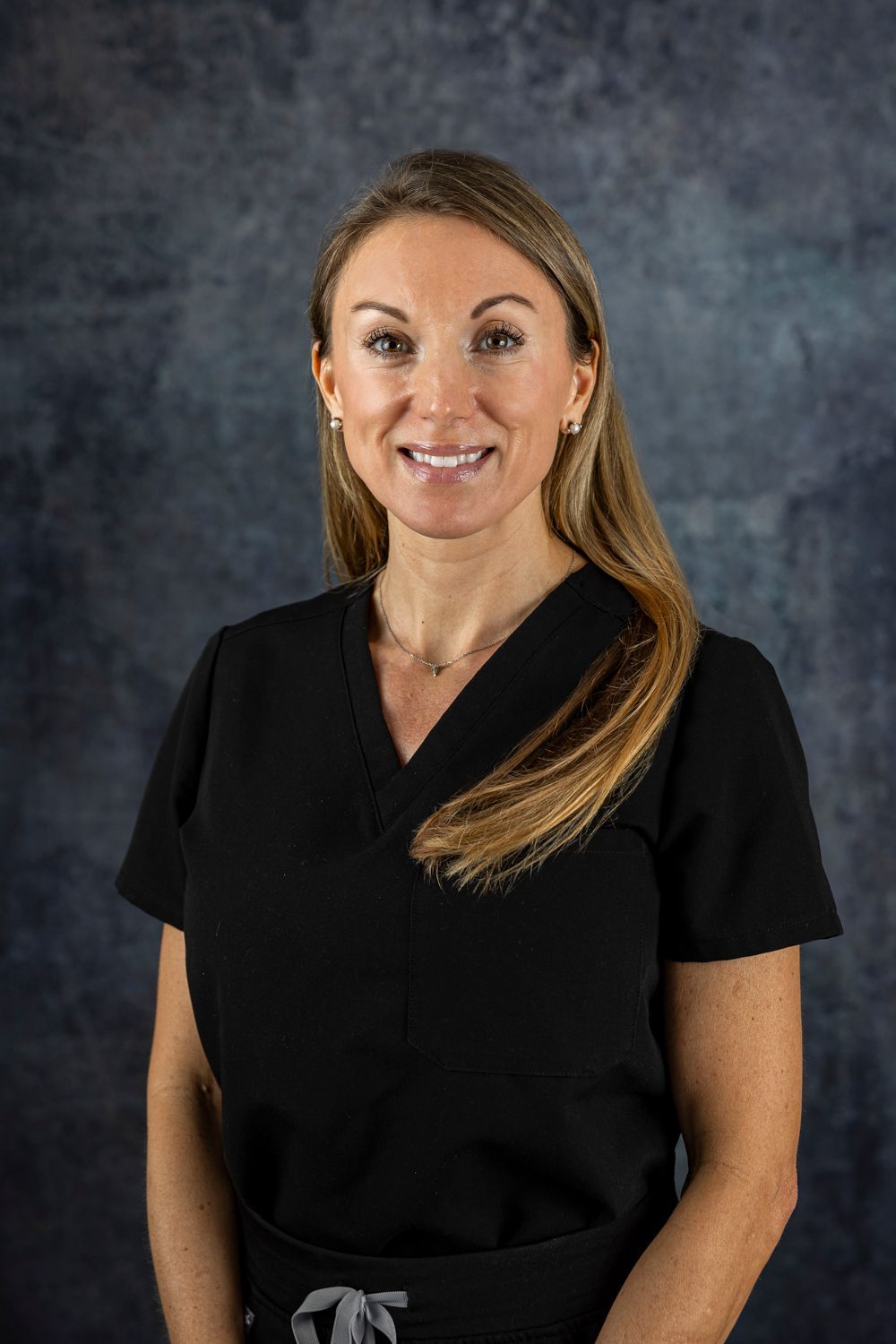 A woman in a black scrub top is smiling for the camera.