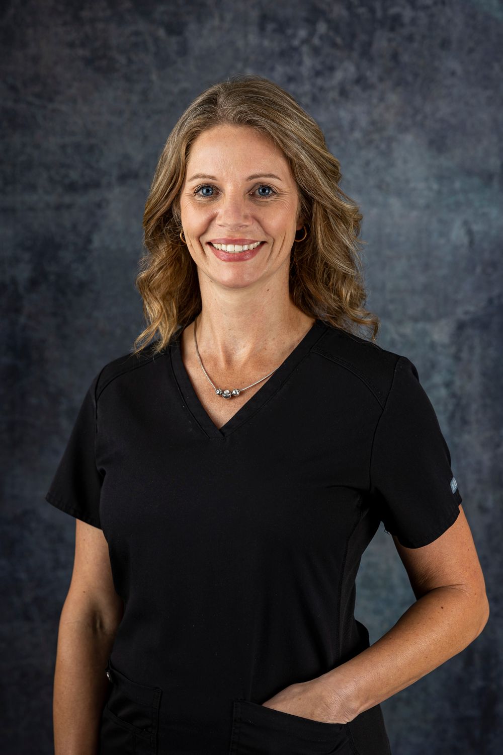A woman in a black scrub top is smiling for the camera.