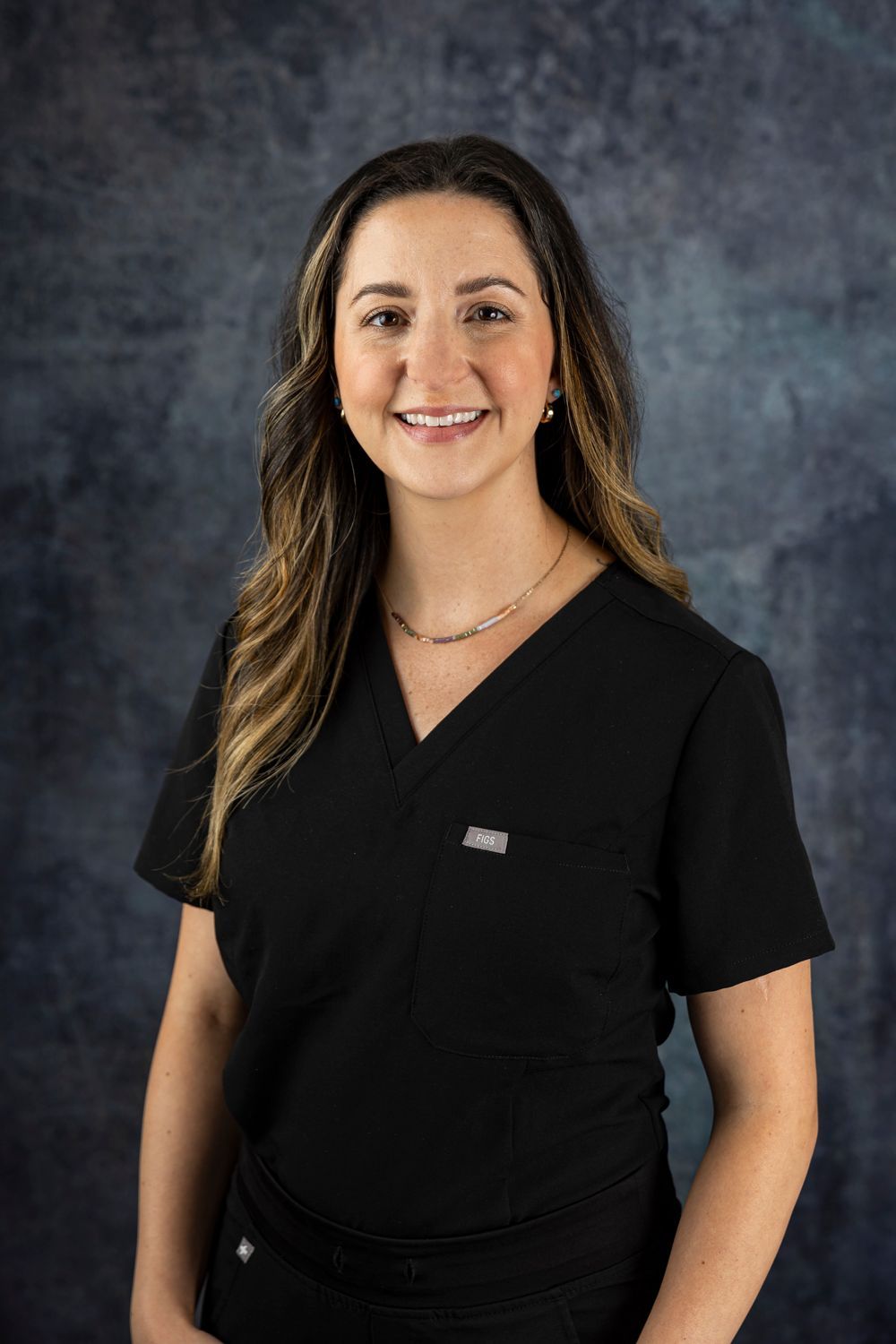 A woman in a black scrub top is smiling for the camera.