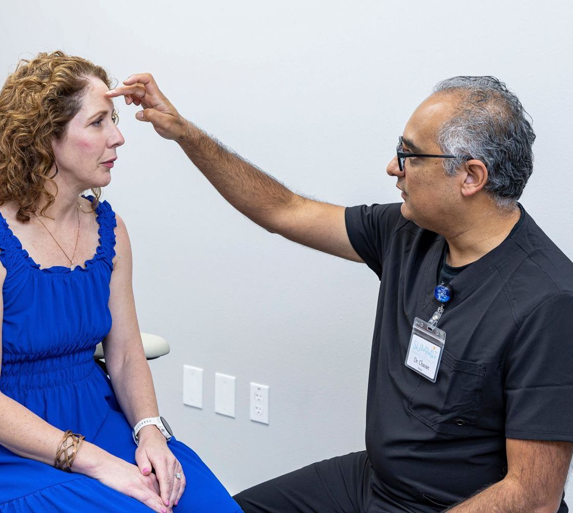 Dr Rahul Chavan is examining a woman 's forehead while she sits in a blue dress at summit dermatology