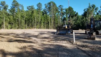 Two excavators on a cleared dirt lot beside a wooded area under a blue sky Two excavators on a cleared dirt lot beside a wooded area under a blue sky