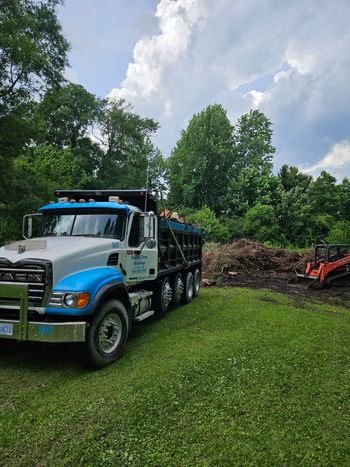 Backhoe clearing rubble beside a red brick house with a steep roof Backhoe clearing rubble beside a red brick house with a steep roof
