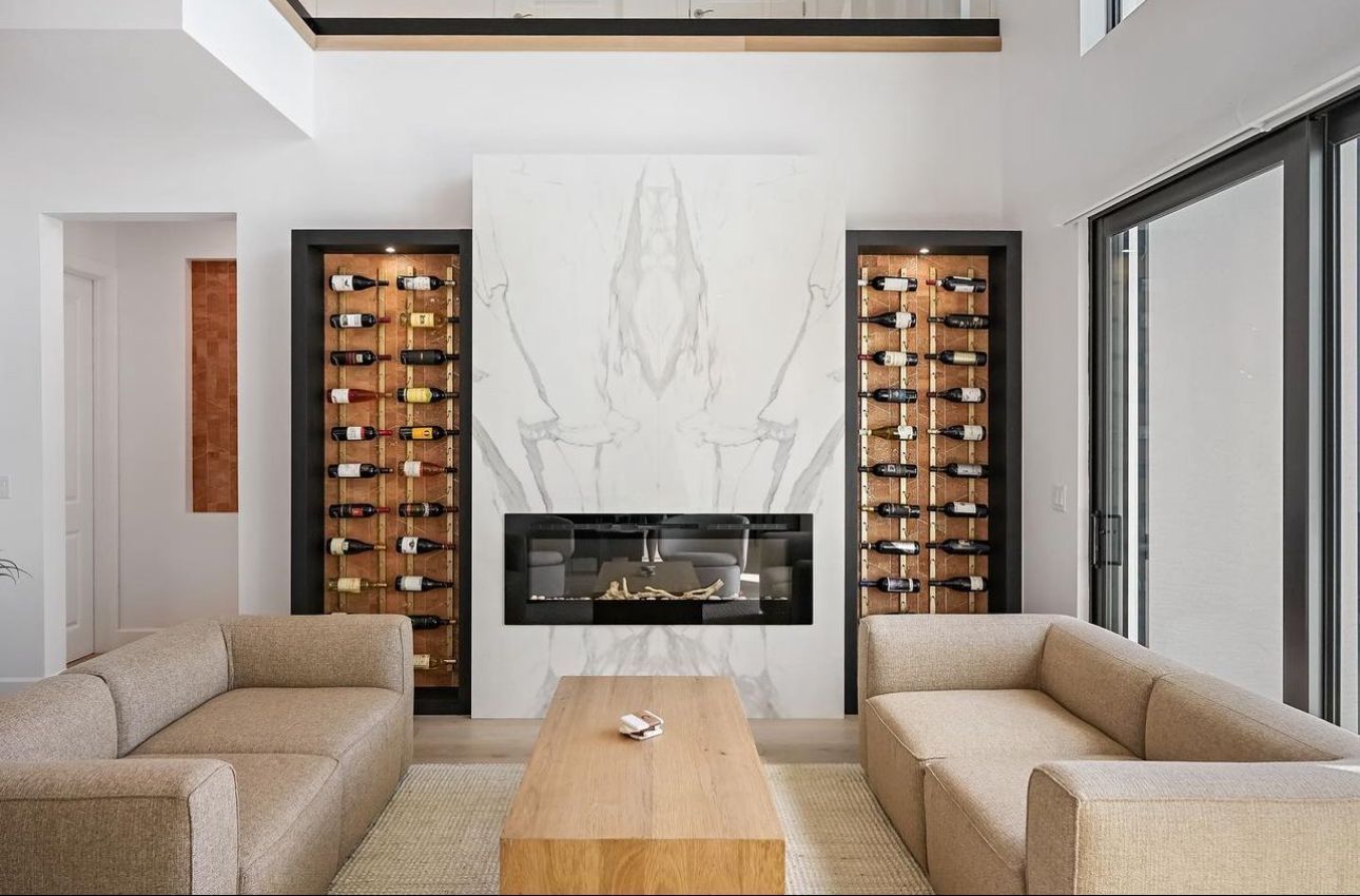 A living room with two couches , a fireplace and a wine rack.