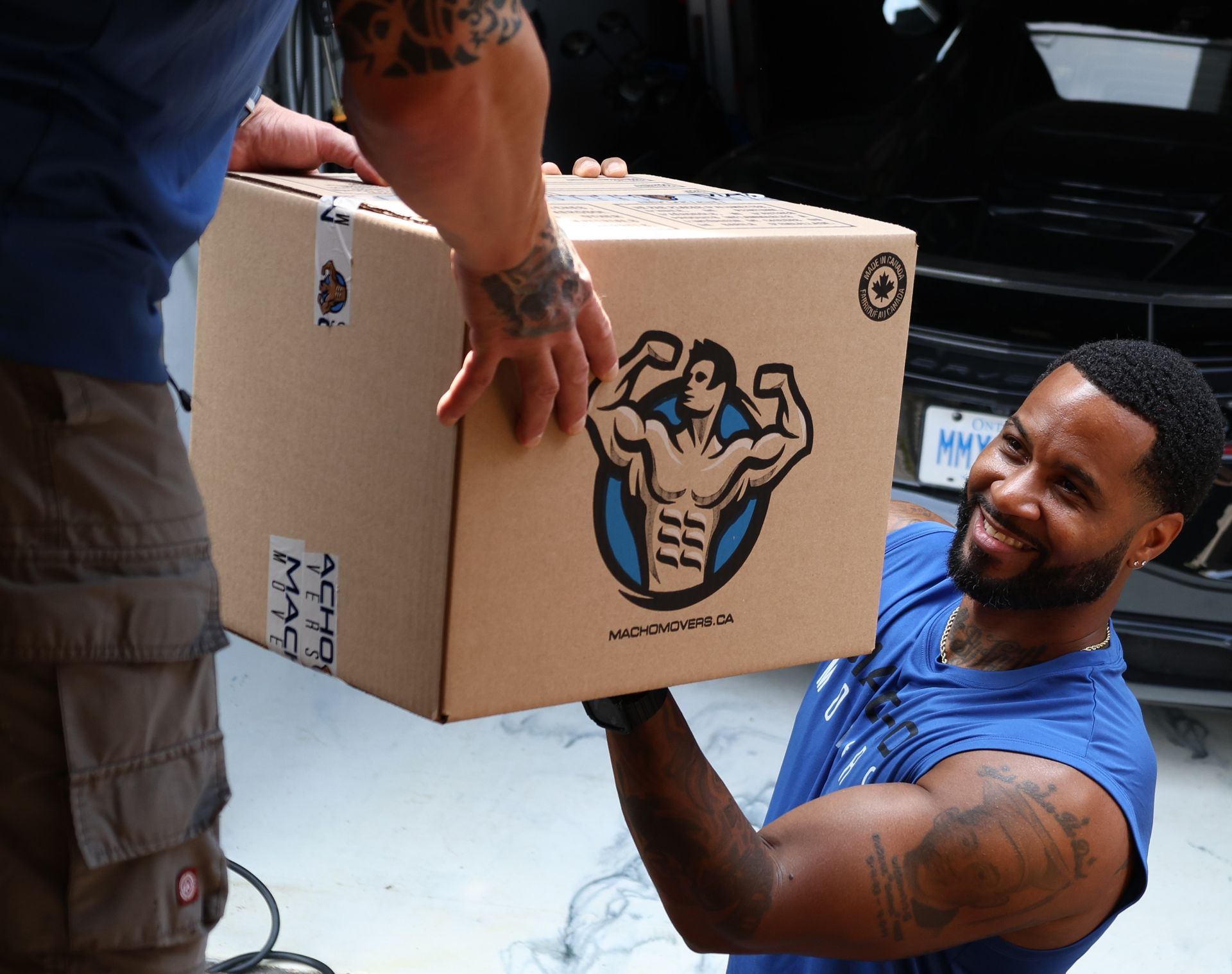Two movers are holding a chair and a rug in front of a van.