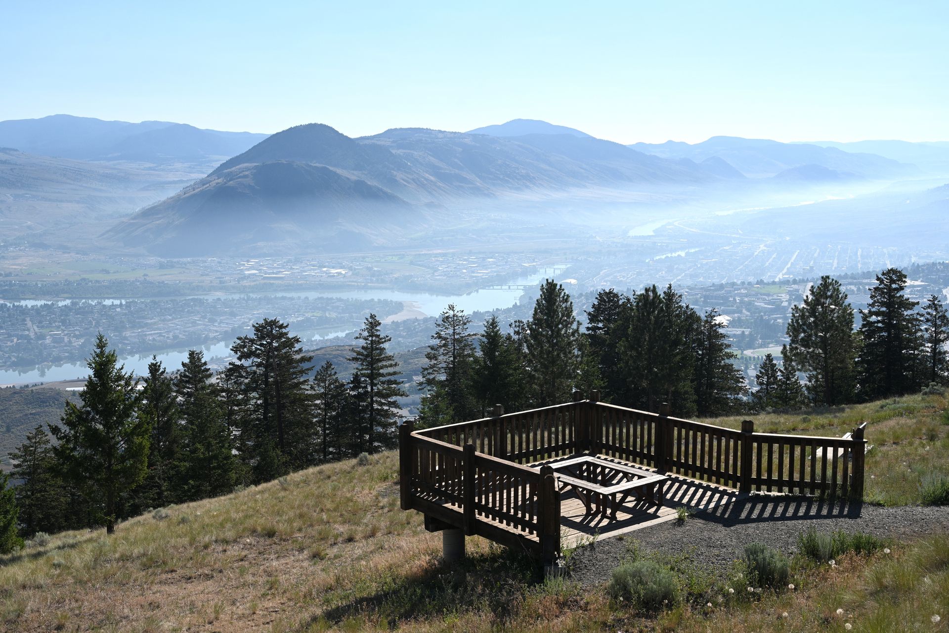 A picnic table is sitting on top of a hill overlooking a city and mountains.