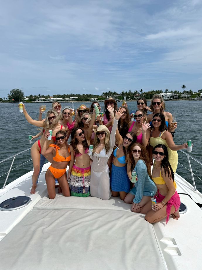 Group of women in swimwear on a boat, posing and smiling on a sunny day.