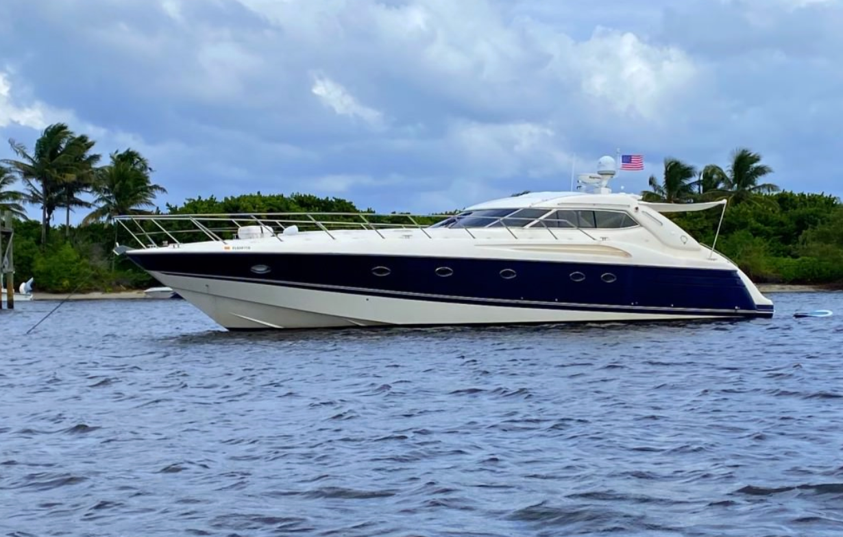 White and navy motor yacht on calm water near palm-lined shore under a cloudy sky