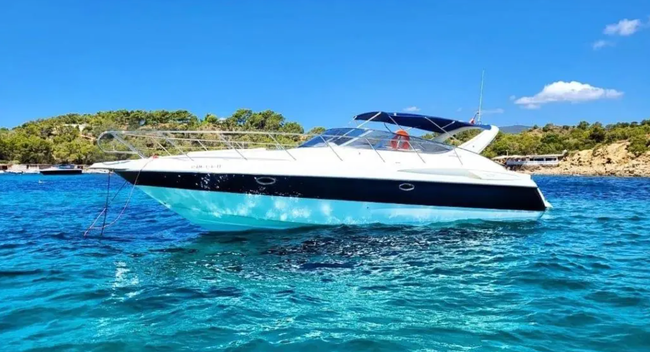 White and black motorboat on blue water, bright sky, coastal backdrop.