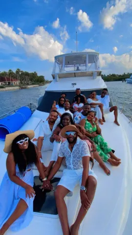 Group of people on a white boat, smiling. Clear sky with fluffy clouds.