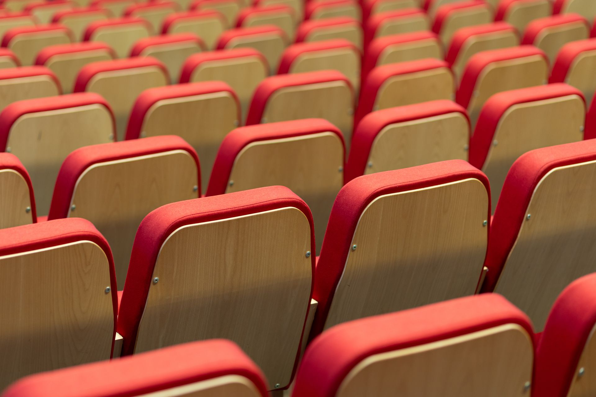 Rows of empty theater seats with red cushions and wooden backs.