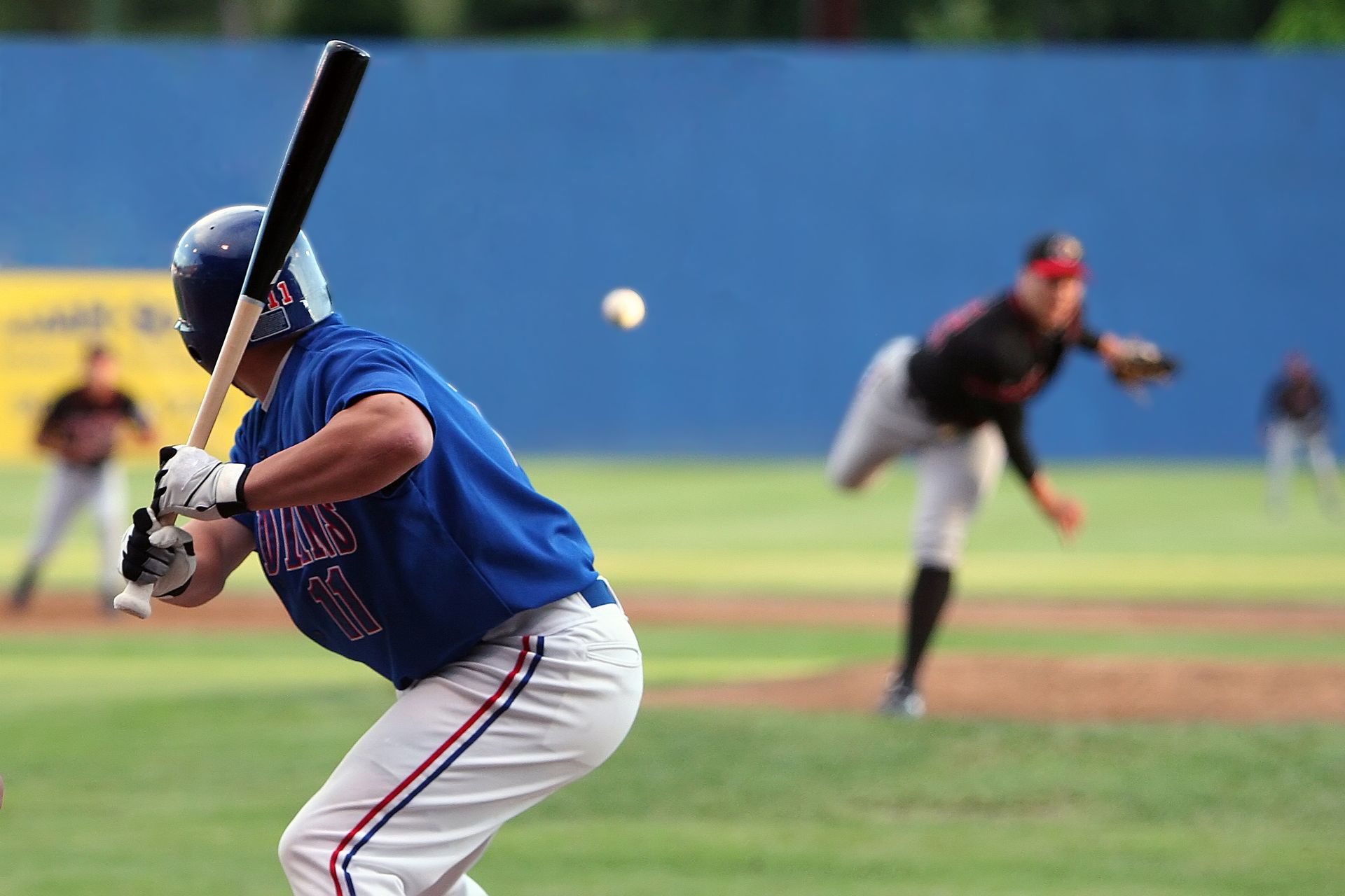 Baseball batter swings at a pitch; pitcher in motion, blue sky.
