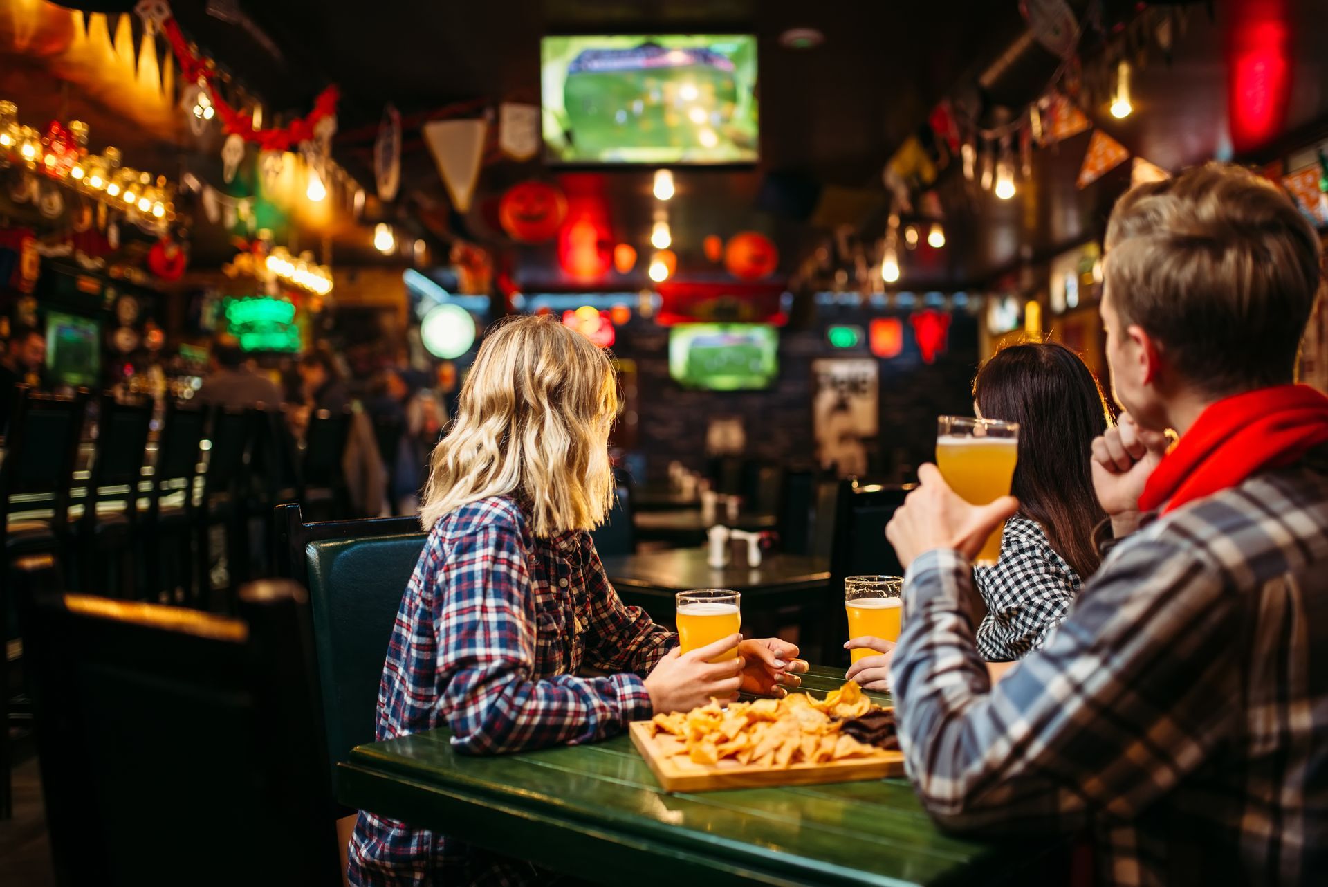 People at a bar, drinking beer and eating snacks. TVs on the wall, warm lighting.