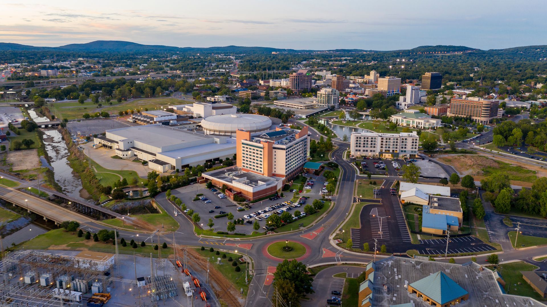 Aerial view of a city with a roundabout in the foreground and buildings and mountains in the distance.