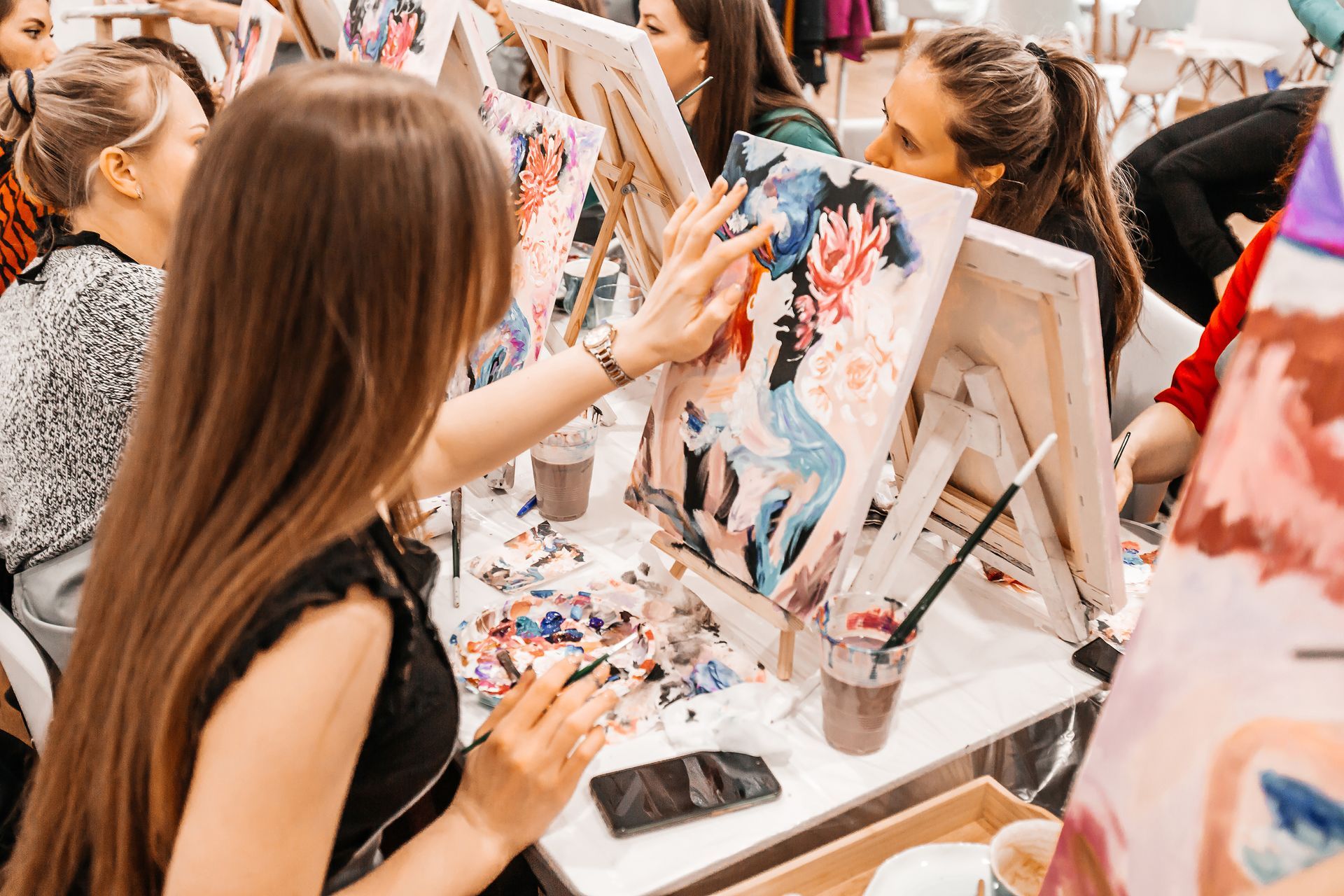 People painting at easels in an art class; close-up of a woman with long hair painting.