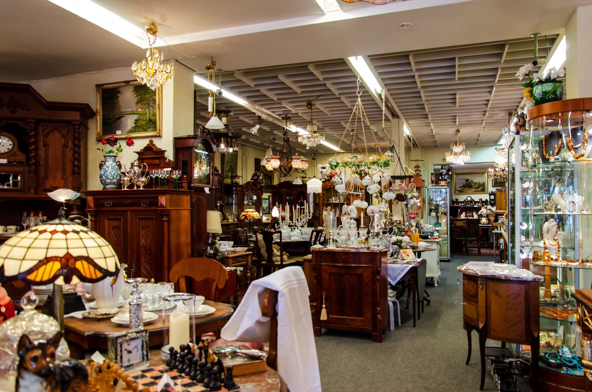 Interior of an antique shop filled with furniture, glassware, lamps, and various decorative items.
