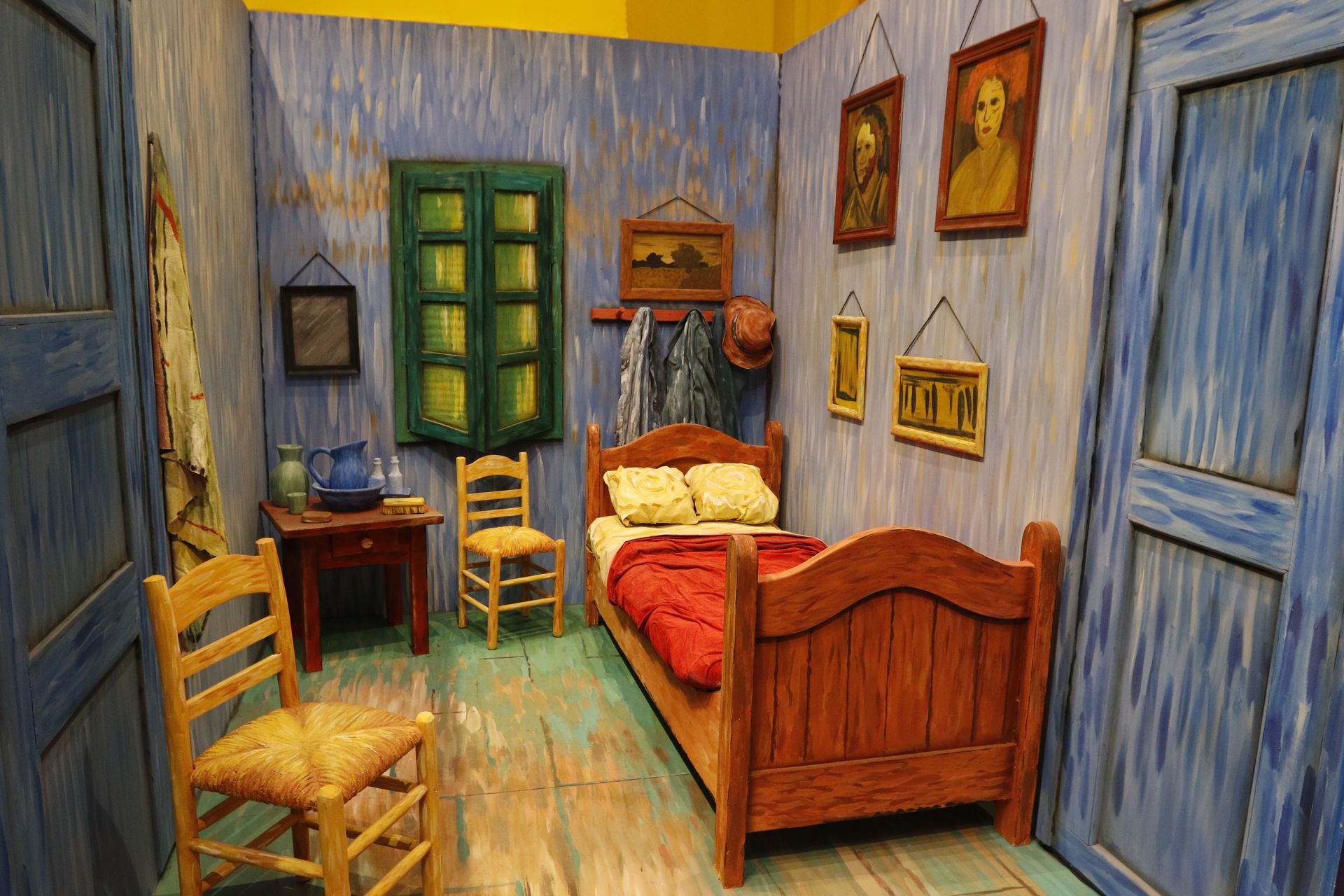 A replica of Van Gogh's bedroom in Arles with blue walls, wooden furniture, and paintings.