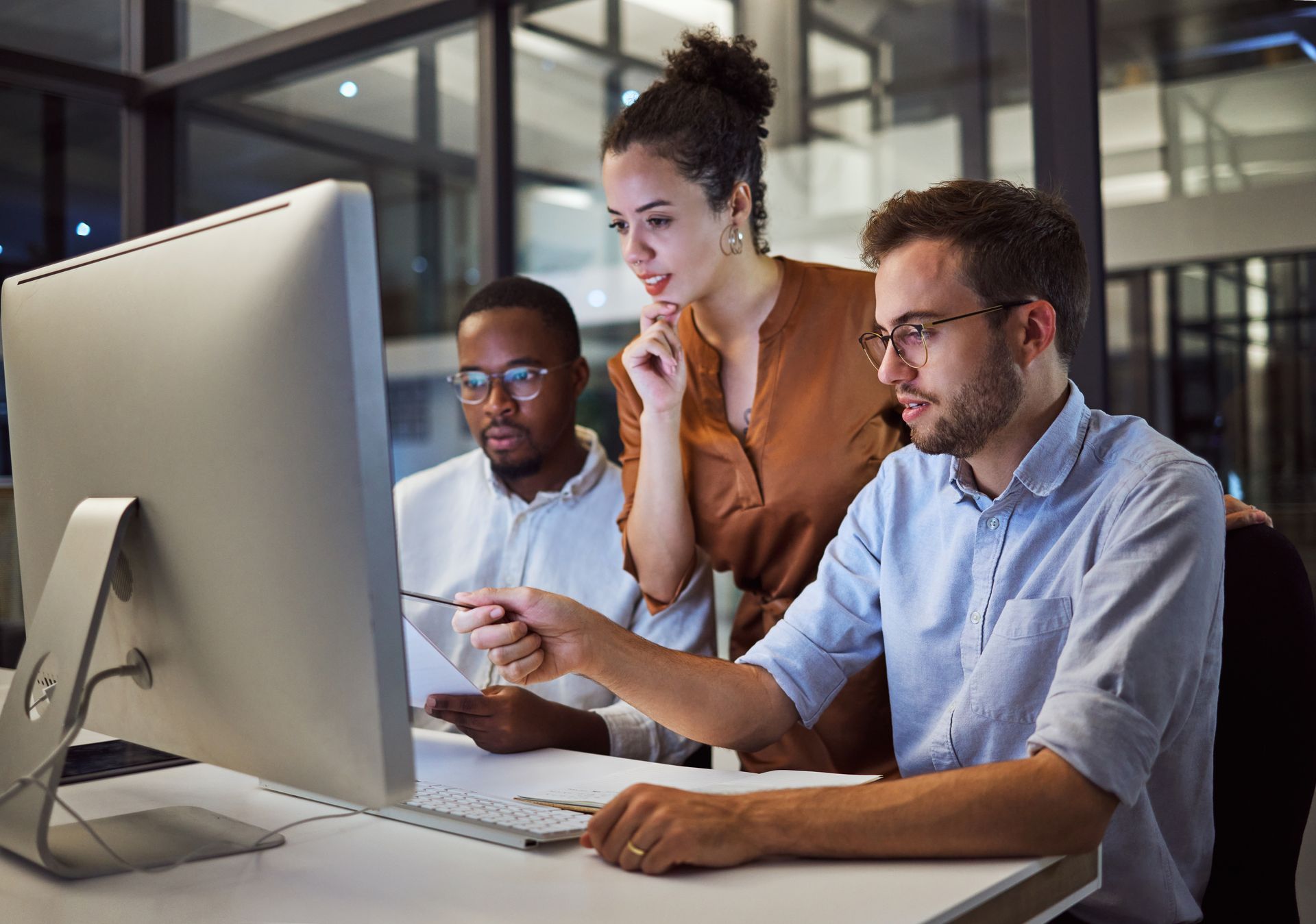 Three colleagues in an office looking at a computer monitor; pointing at screen.