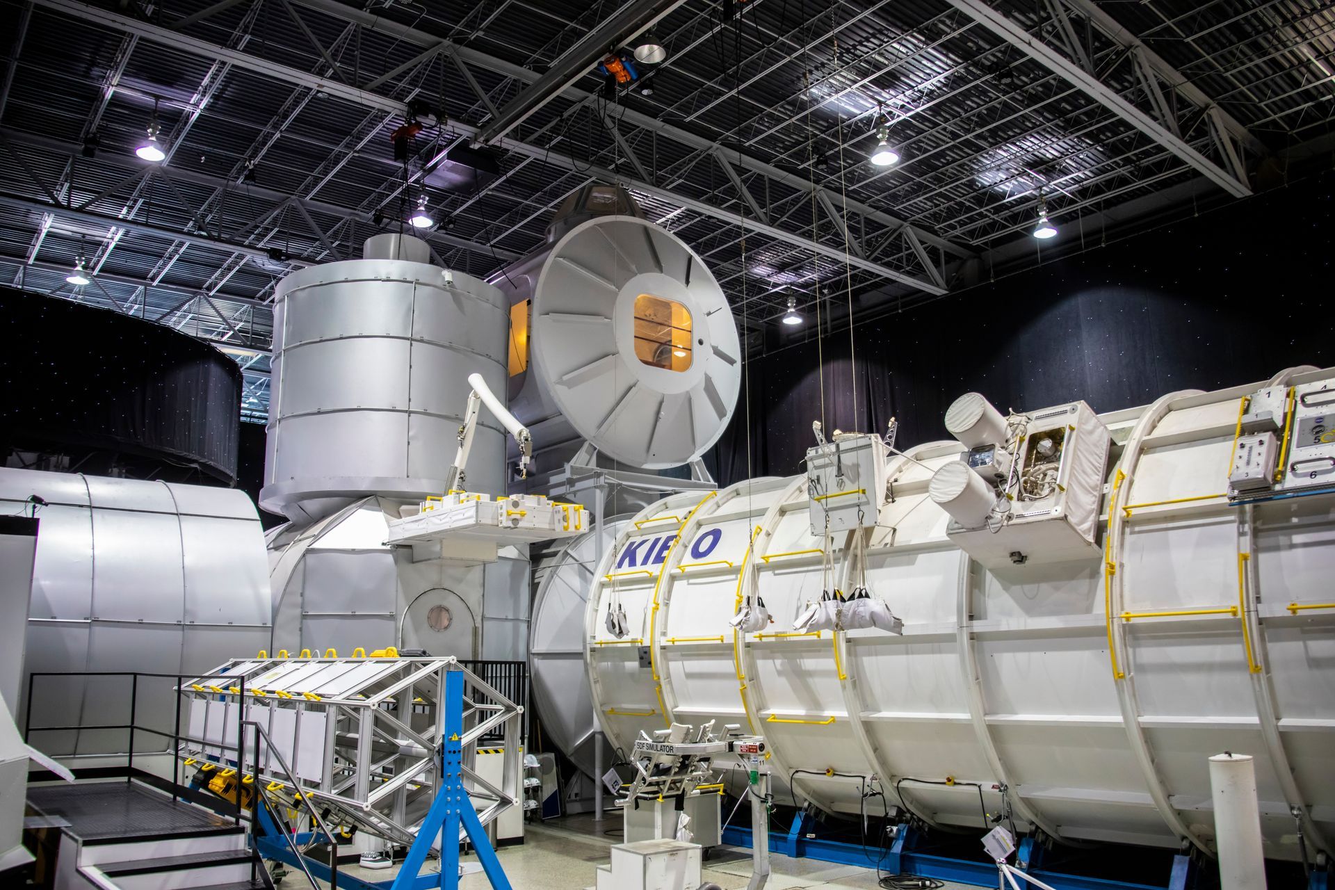 A mockup of a space station interior, with white modules, robotic arms, and complex equipment.