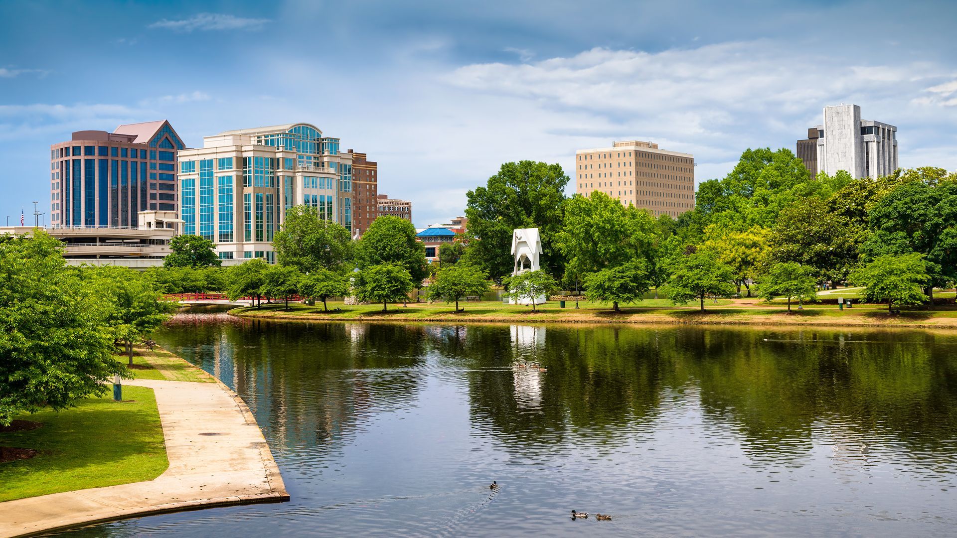 City skyline with buildings, trees, and a lake. Sunny day.