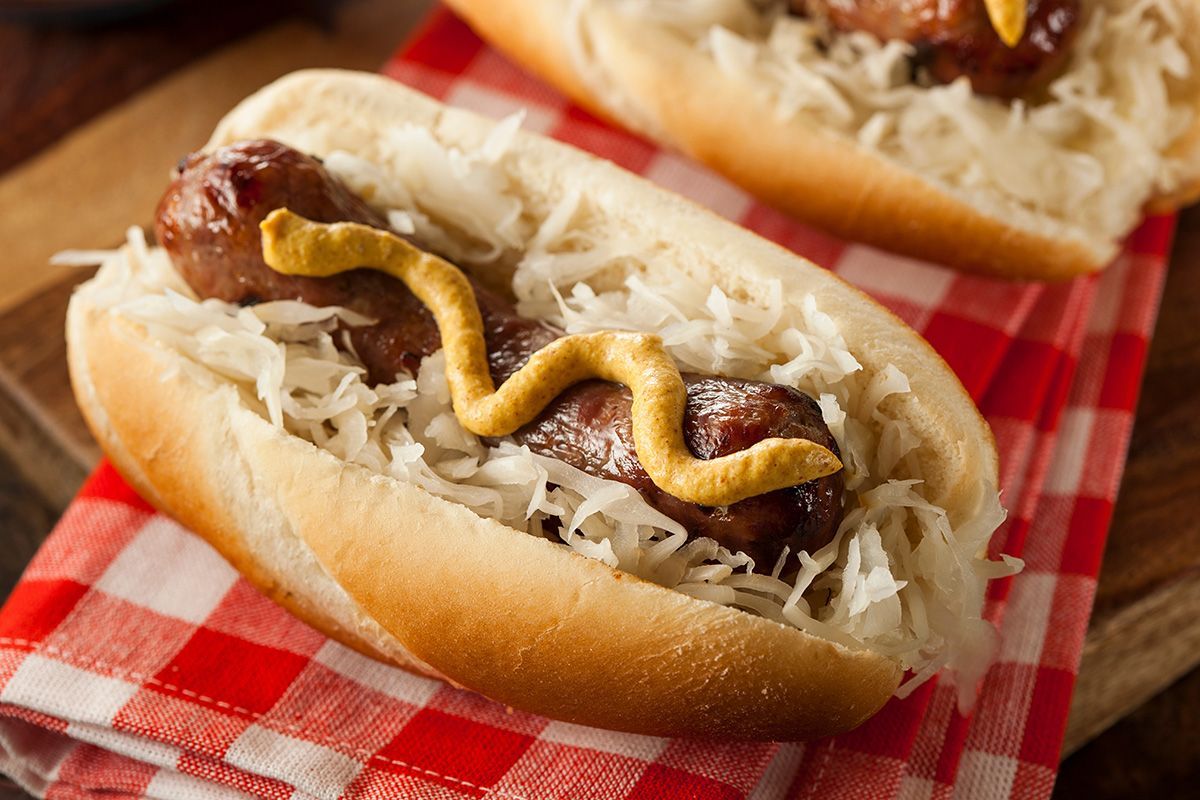 a bratwurst on a bun with mustard and sauerkraut on a checkered napkin .