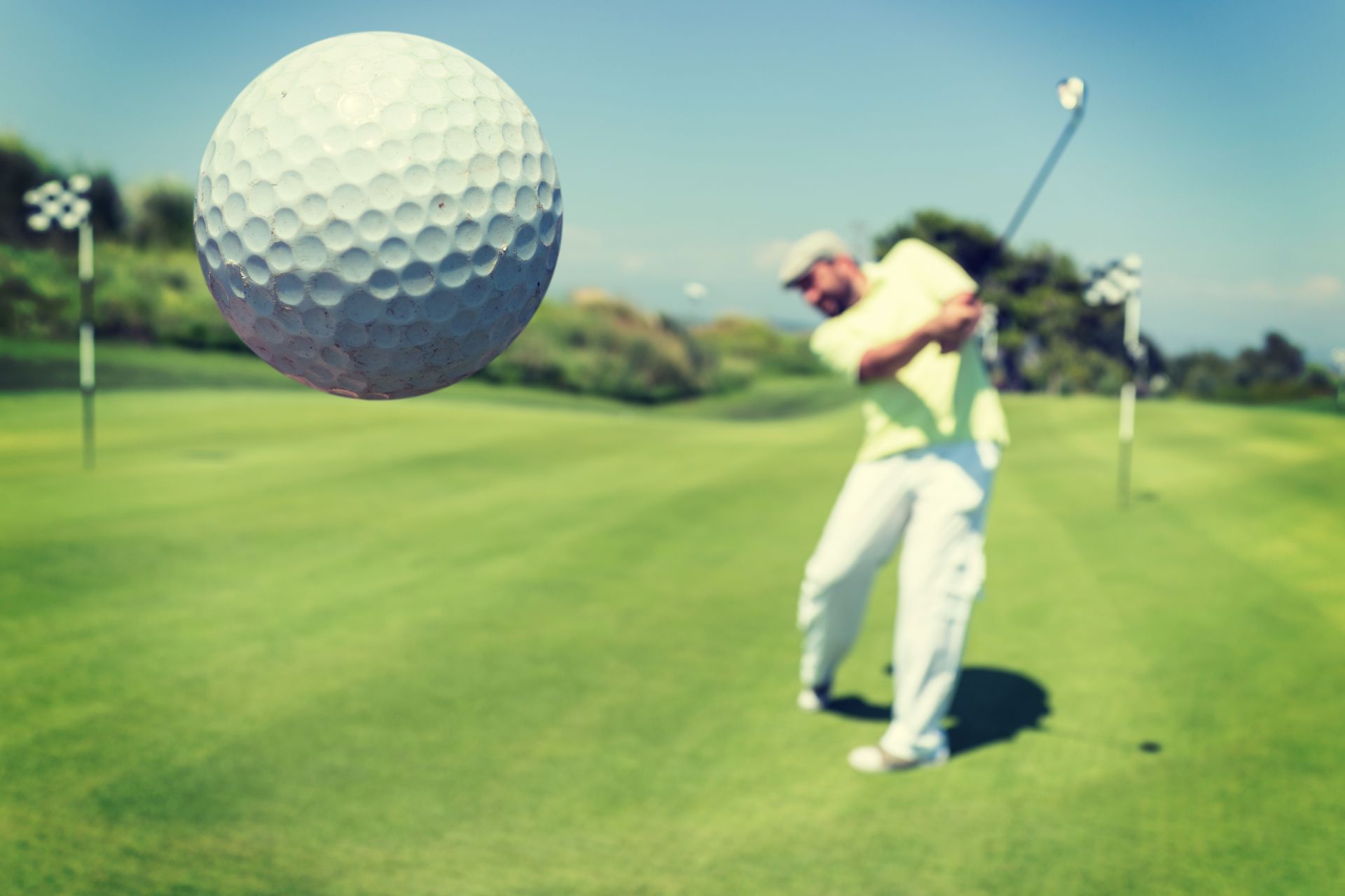 Golf ball mid-air above golfer swinging club on a green course.