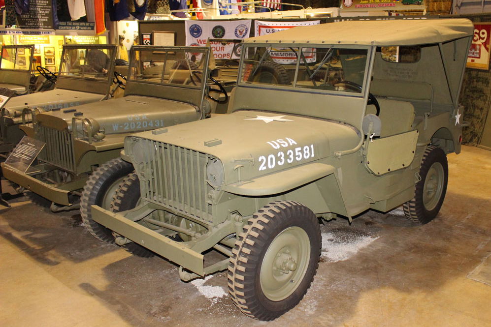 Three olive drab military jeeps displayed indoors.