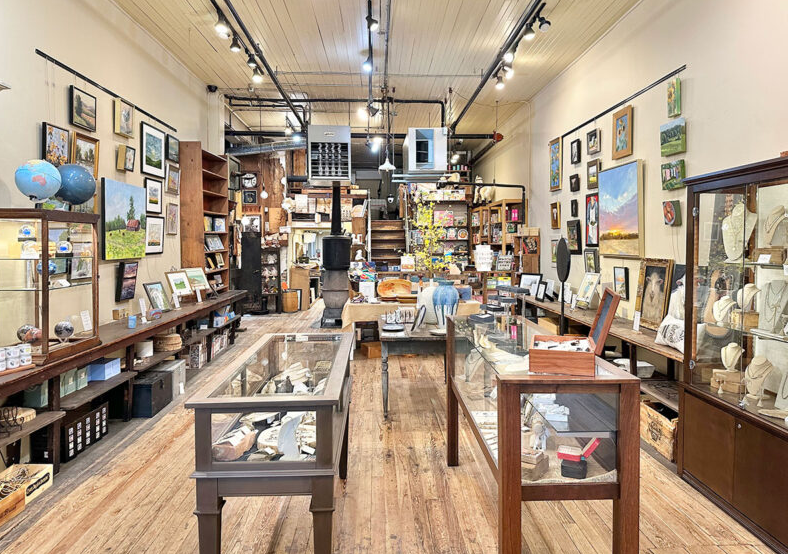 Interior of a retail store with wooden floors, display cases, artwork, and various merchandise.