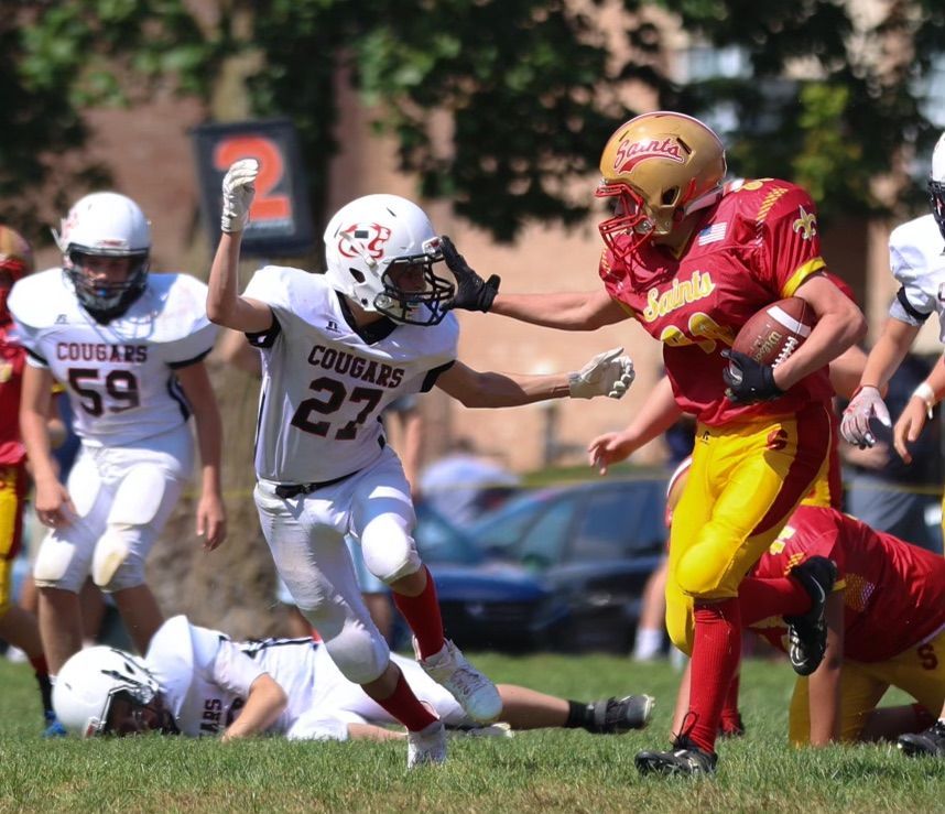 Football player in red and gold runs with the ball as two defenders in white try to tackle him.