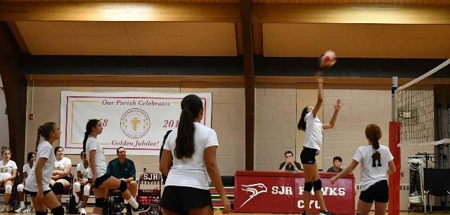 Indoor volleyball game with players at the net and a ball in play near the right side of the court