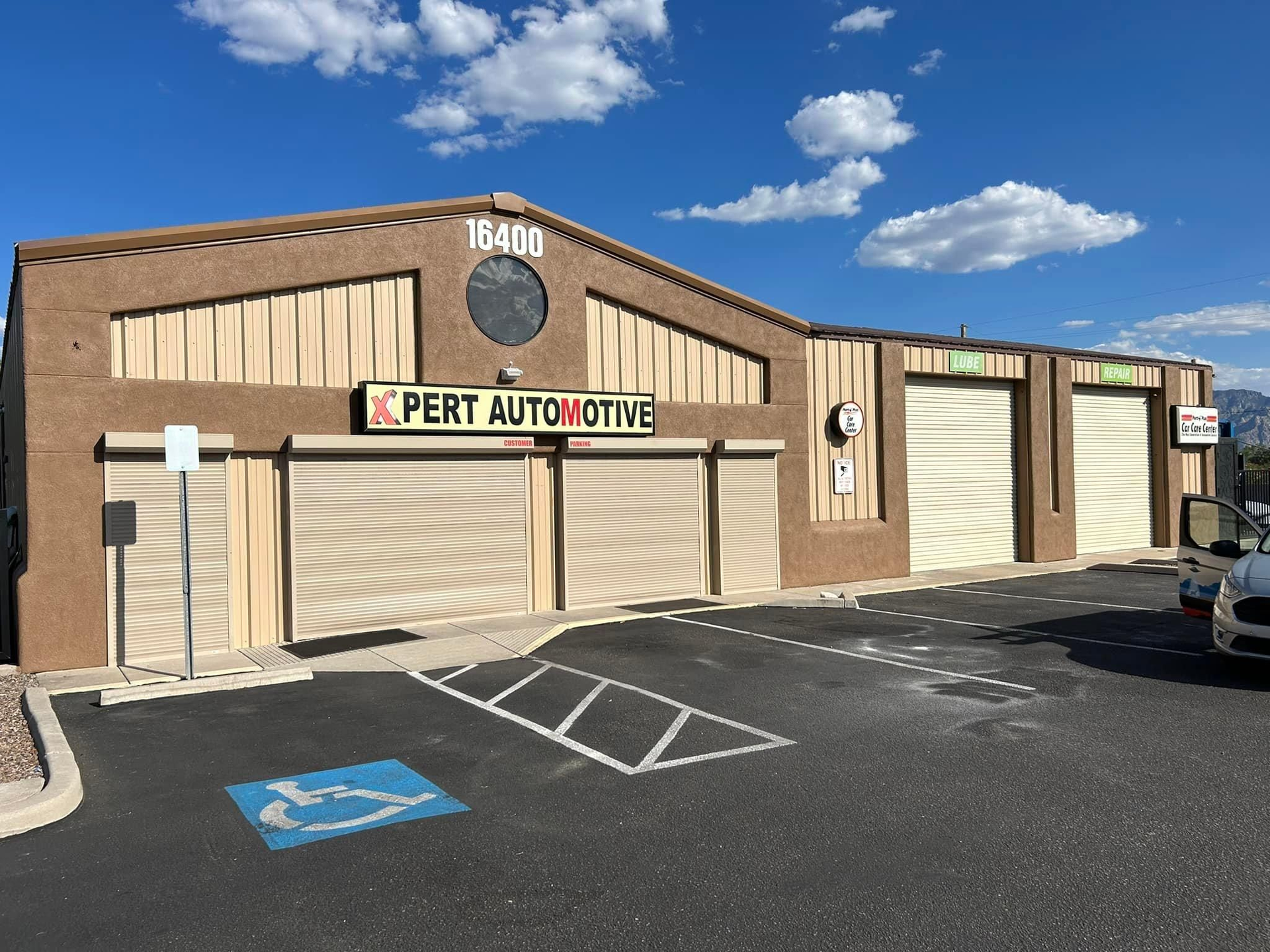 Pert Automotive shop with tan exterior, roll-up doors, and a parking lot with a handicap space.