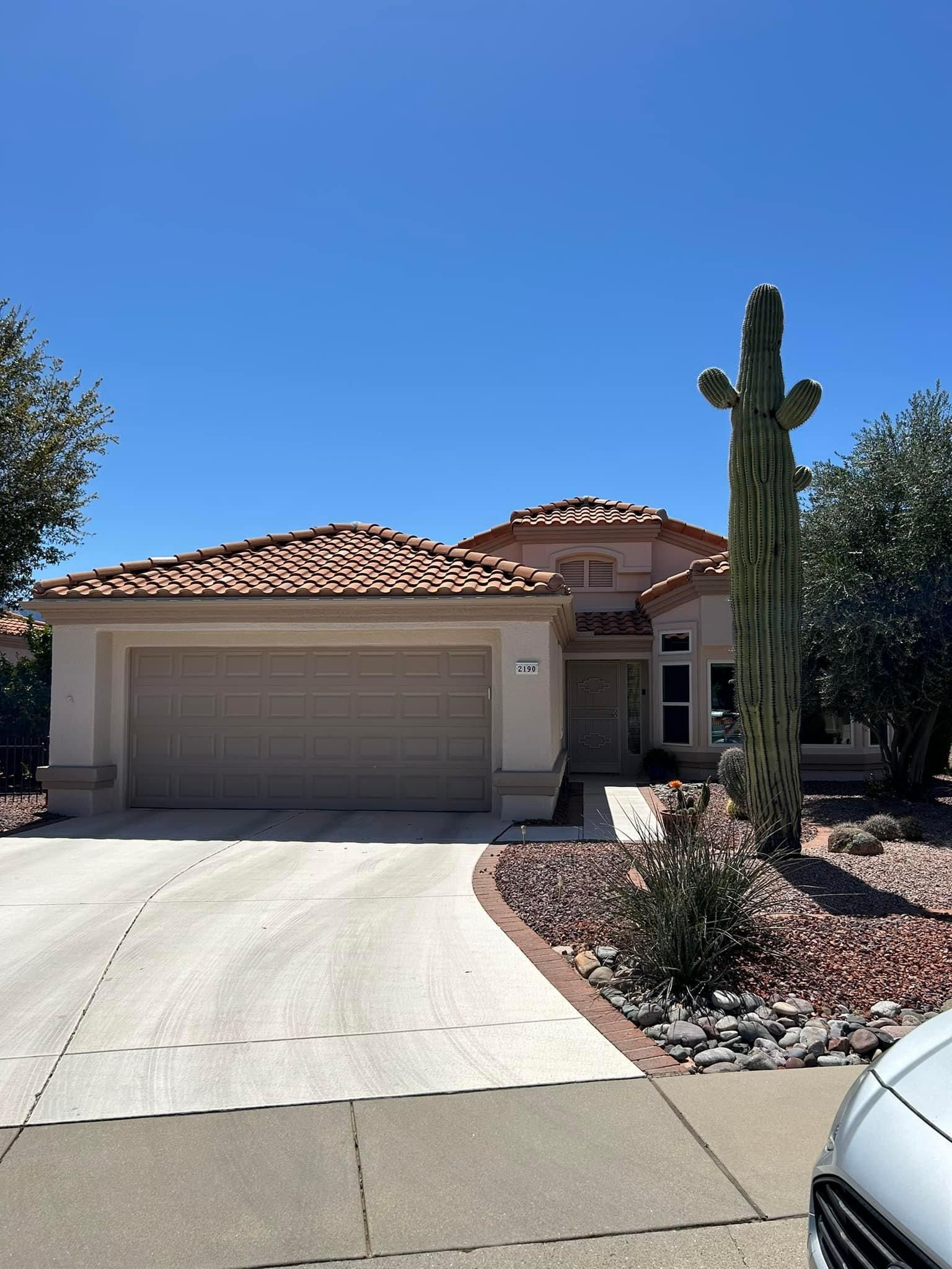 Tan stucco house with a beige garage door and tile roof against a mountain backdrop under a cloudy sky.