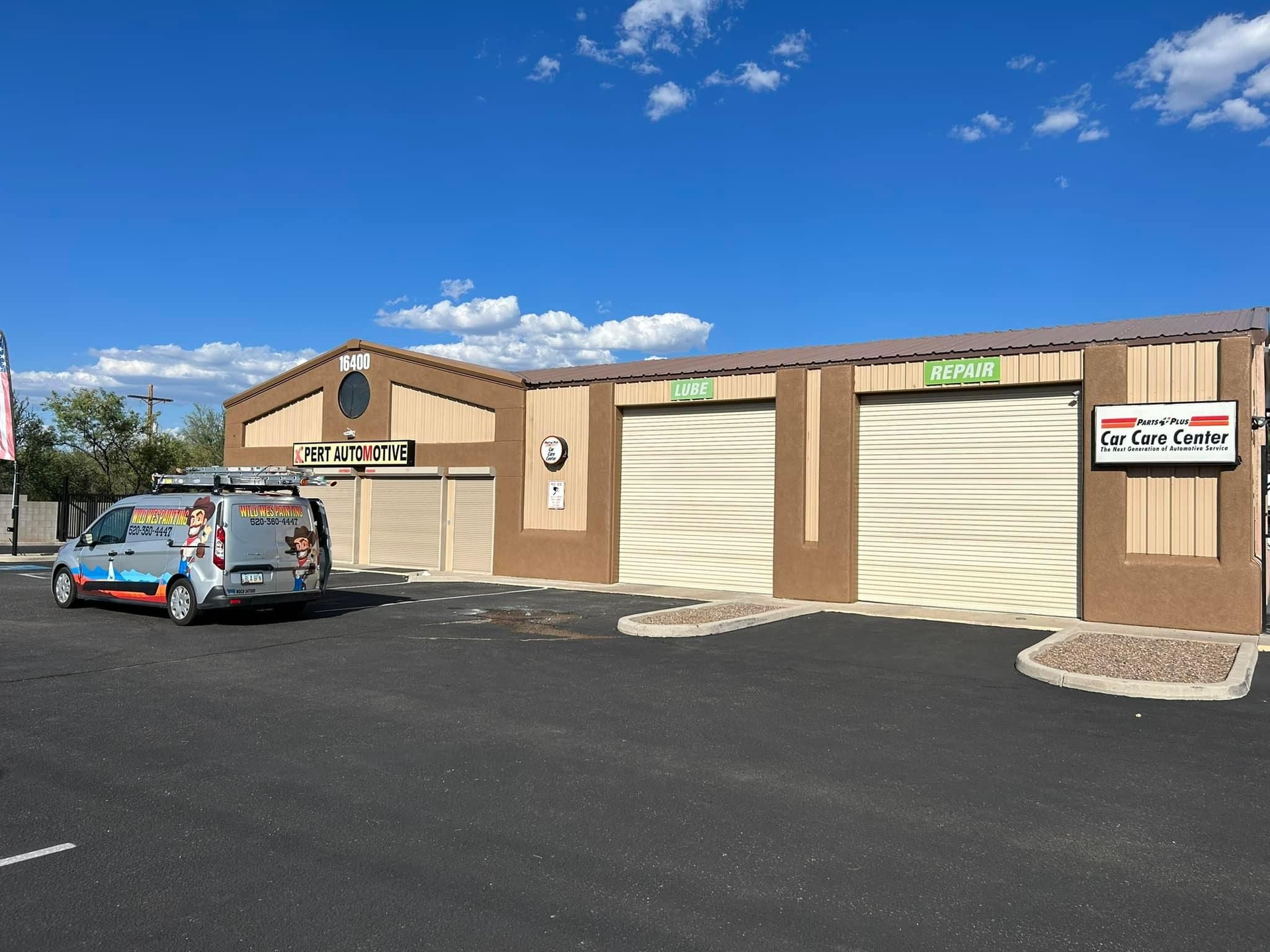 A van is parked in front of a beige commercial building with two garage doors. The sign says 