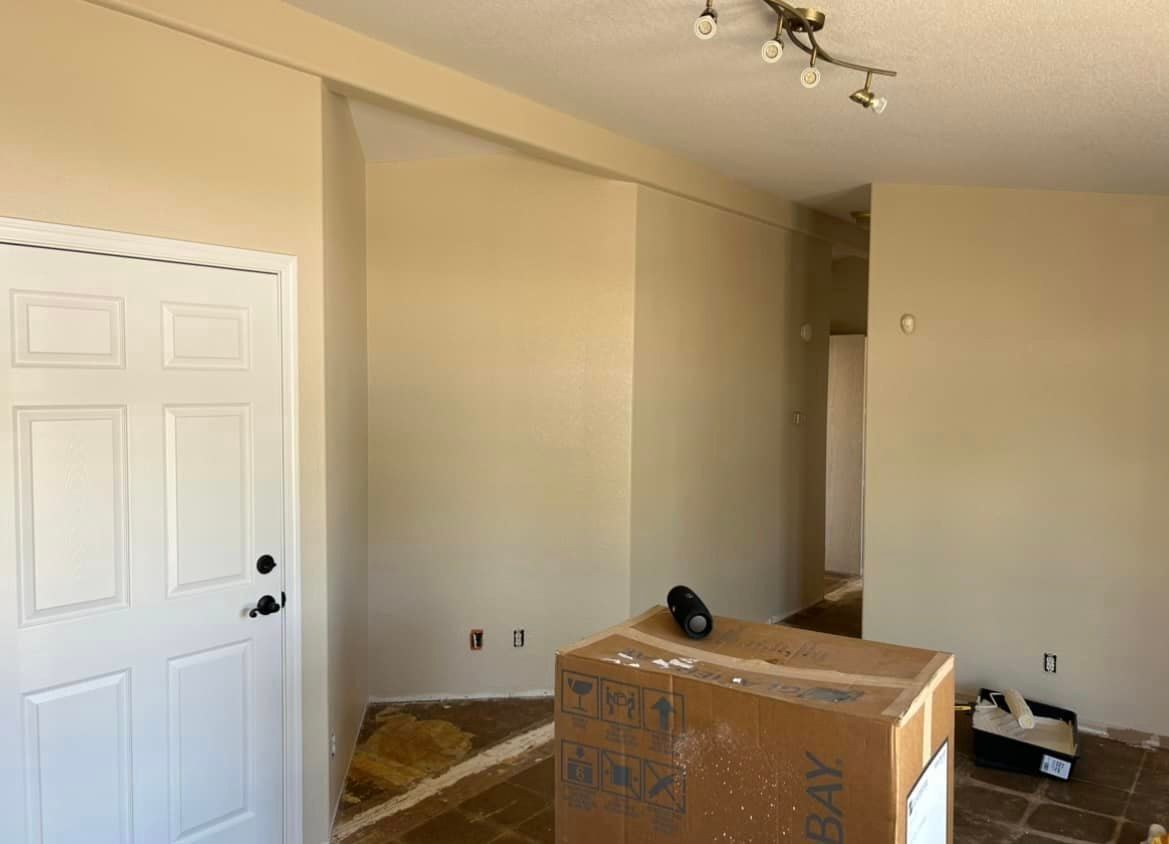 Interior view of a room with a white door, beige walls, and a large cardboard box on the floor; construction is in progress.