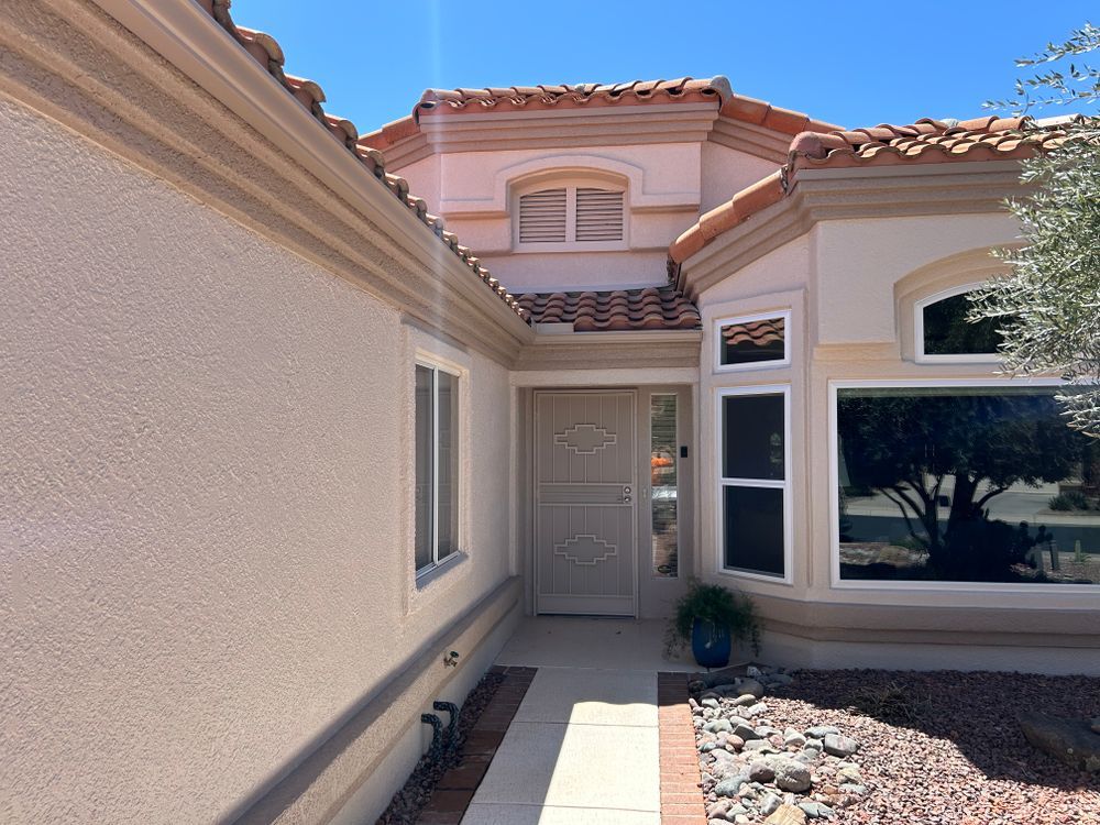 Exterior view of a beige stucco house with red tile roof, doorway, windows, and a walkway.