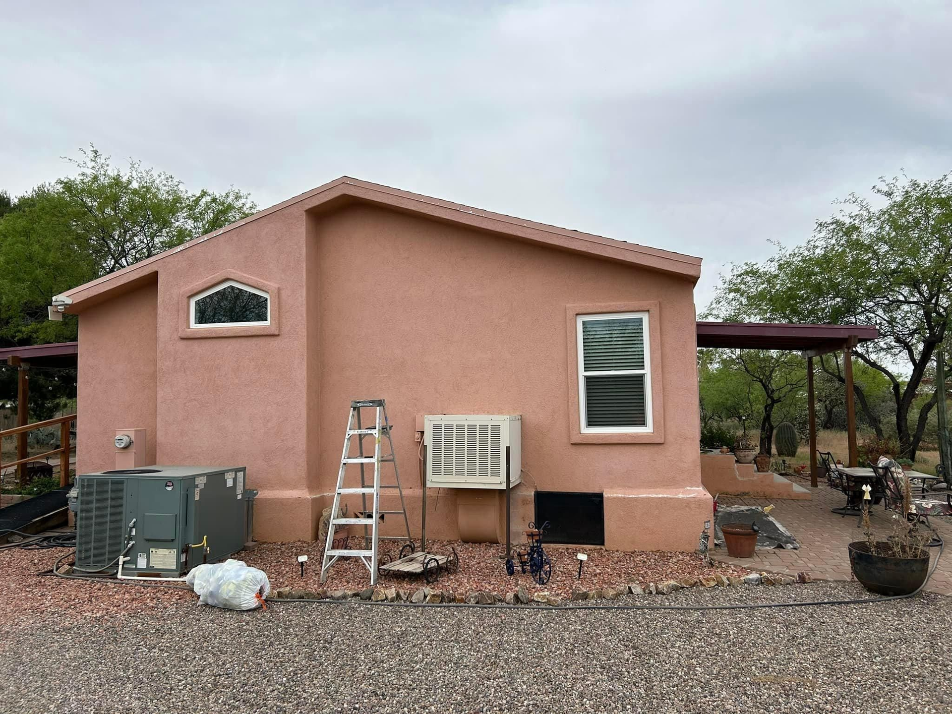 A pink stucco house with a ladder, air conditioning units, and a covered patio.