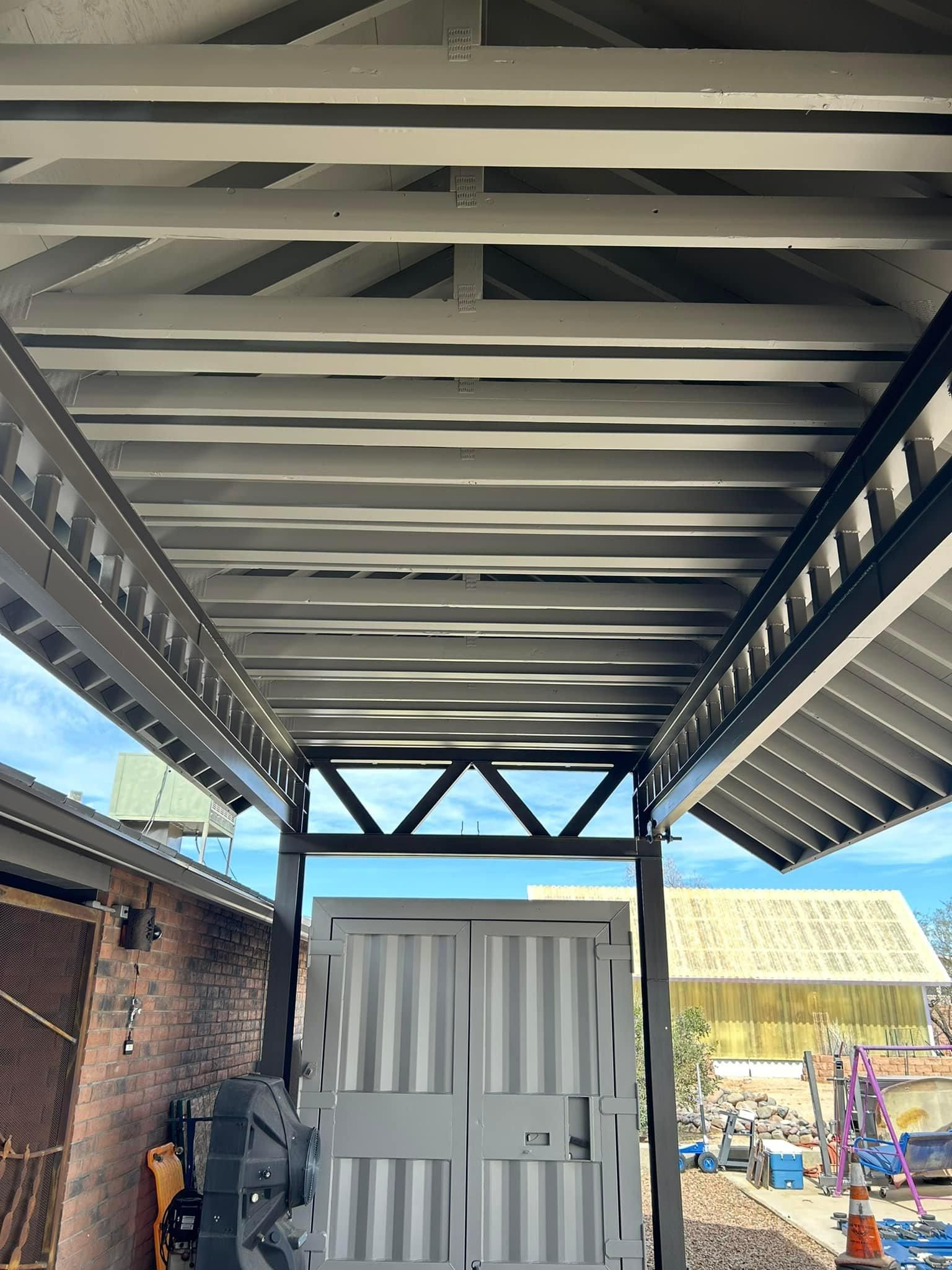 View of a metal awning painted gray, supported by black posts. The awning covers a double door and building.