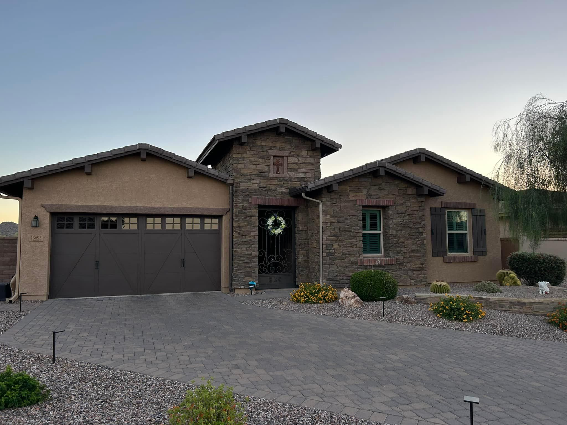 A single-story home with a stone facade and brown garage door, set in a gravel-covered yard.