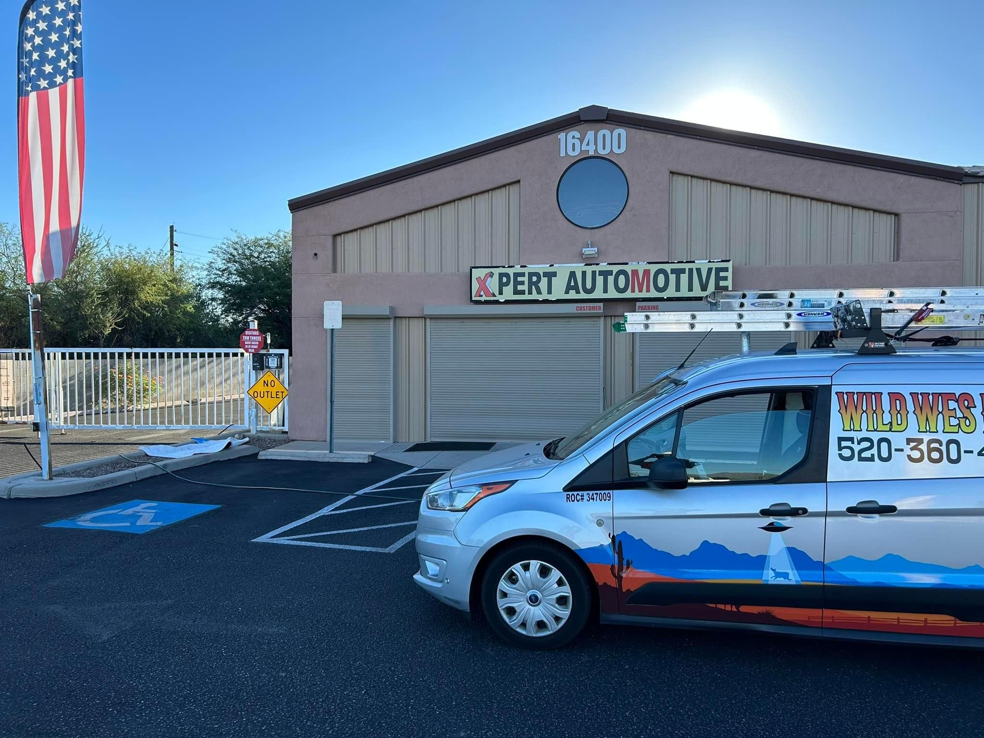 A silver van parked in front of Xpert Automotive. An American flag flies to the left of the building.