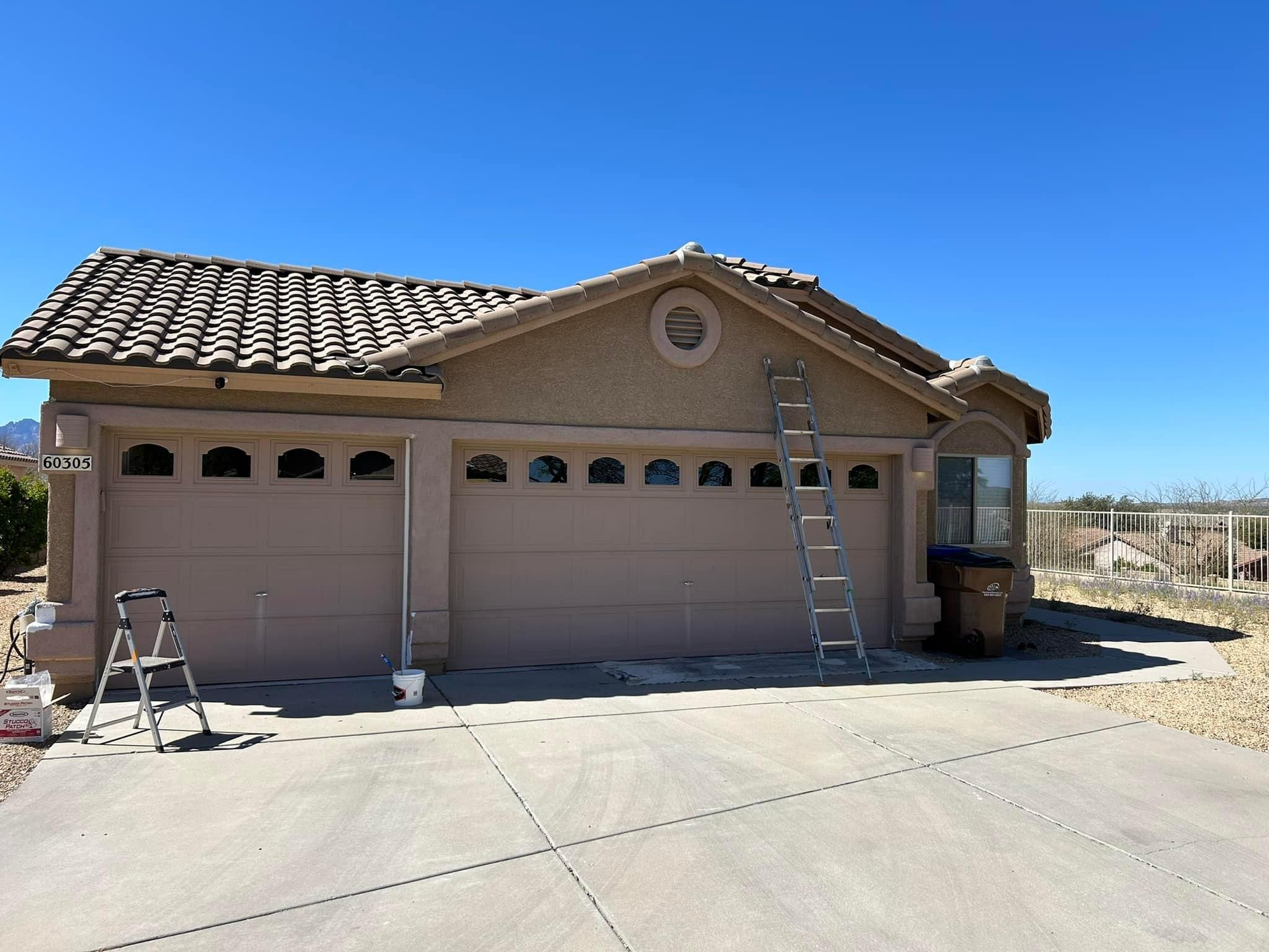 Tan stucco house with garage doors and a ladder propped against it, on a clear, sunny day.