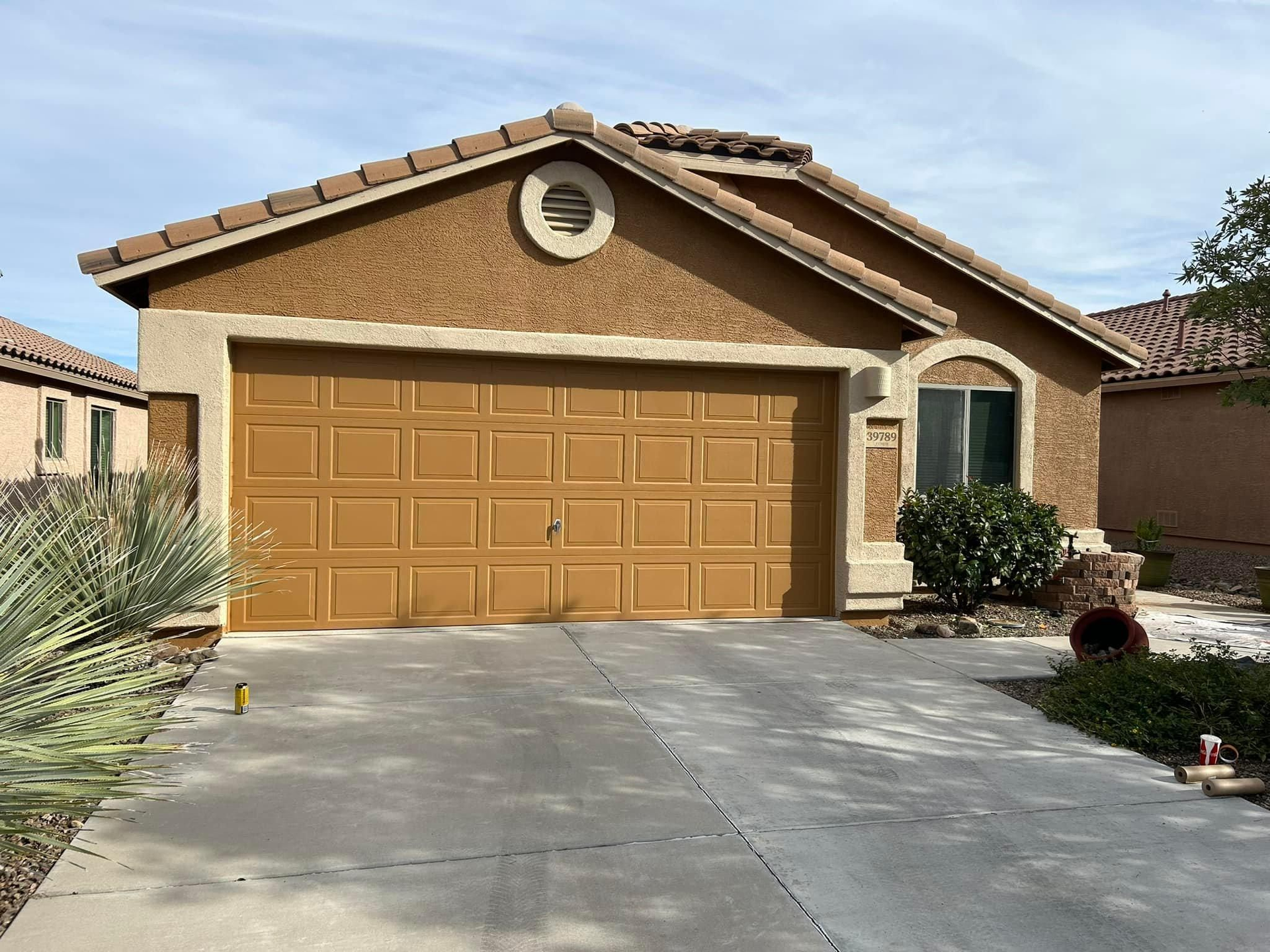 Tan stucco house with a brown garage door, set in a sunny environment.