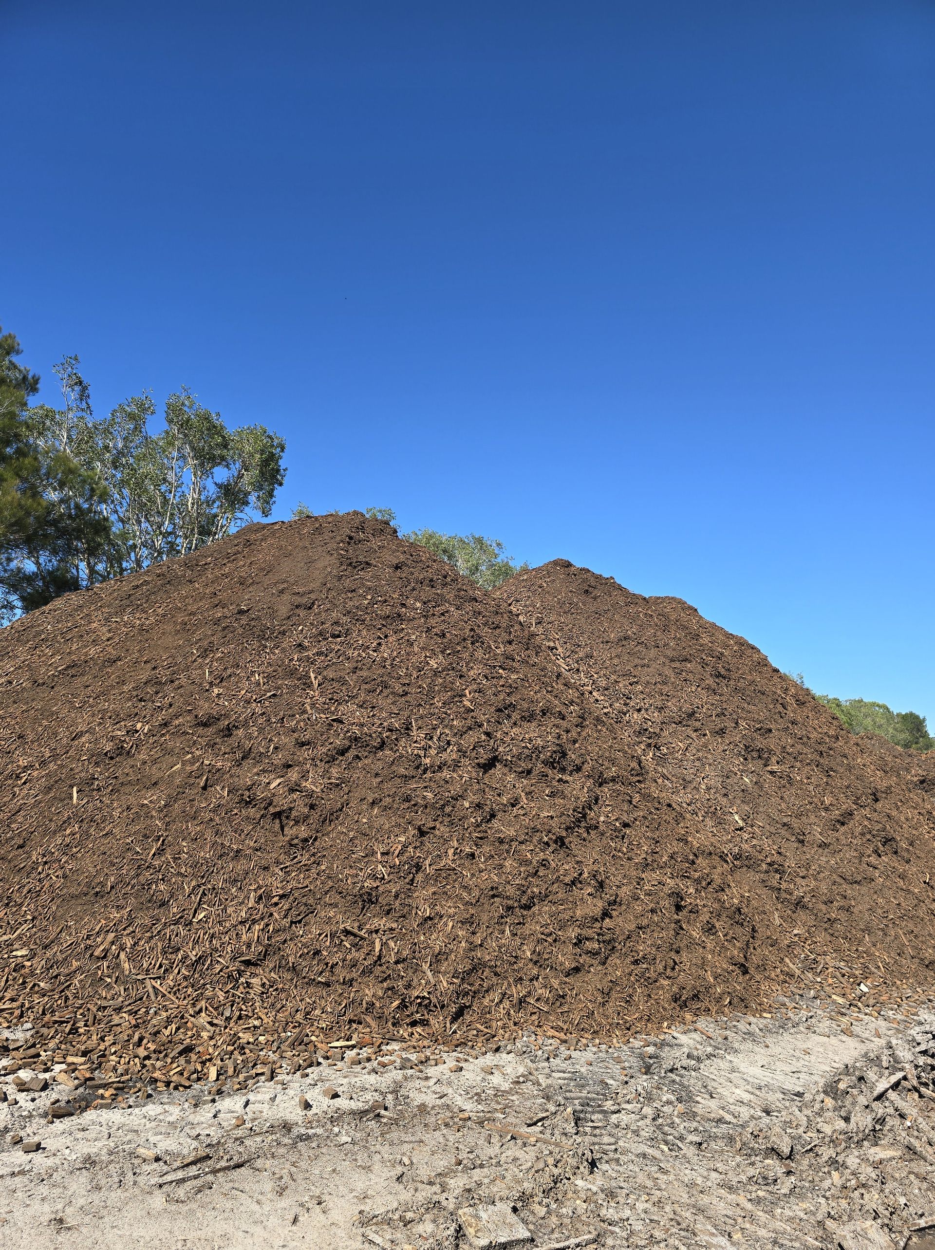 Pile of brown mulch against a blue sky — Coastal Sand Soil & Mulch in Craignish, QLD