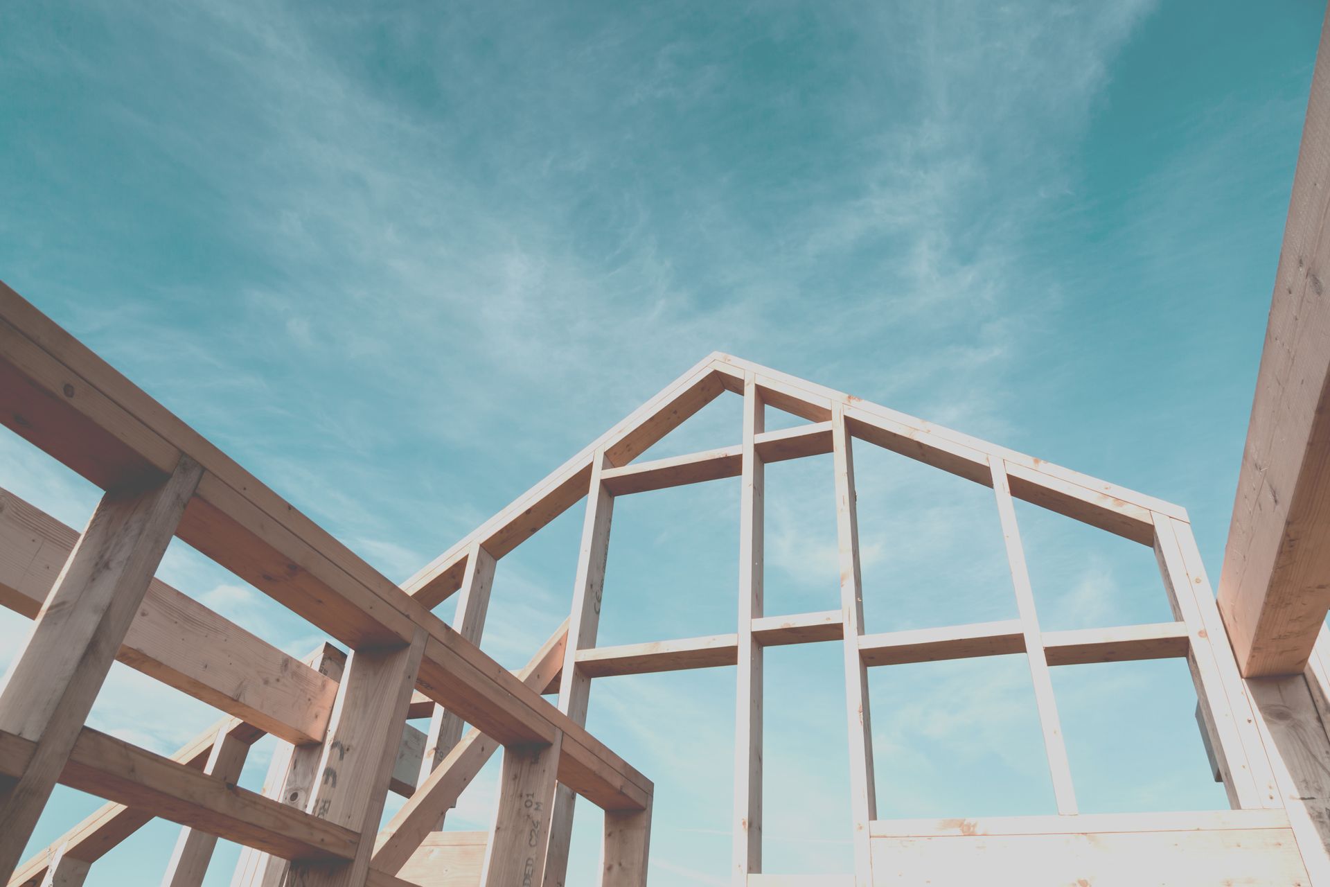 Wooden frame structure of a house under construction against a clear blue sky.