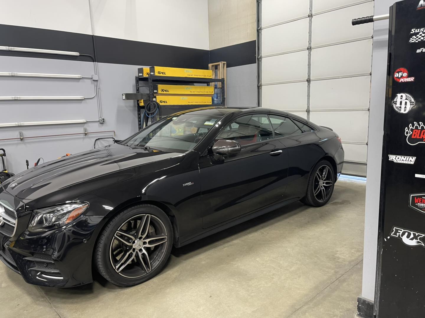 A black car is parked in a garage next to a sign.