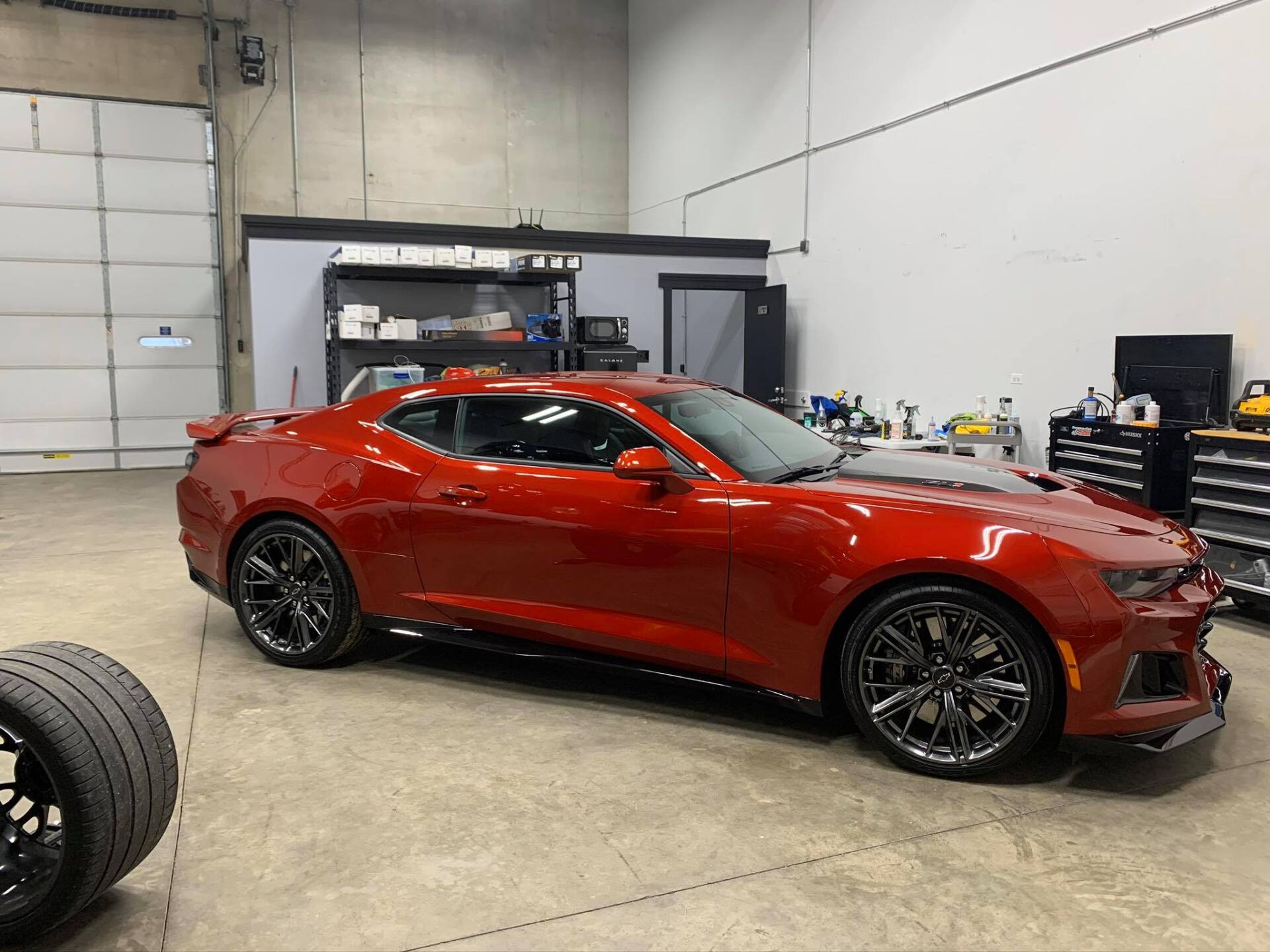 A red car is parked in a garage next to tires.