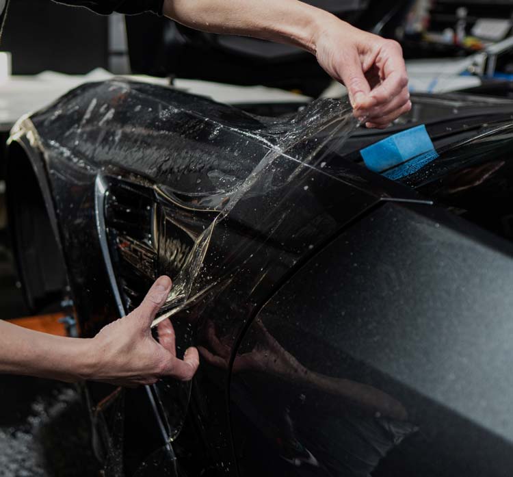 A person is wrapping a car with plastic wrap.